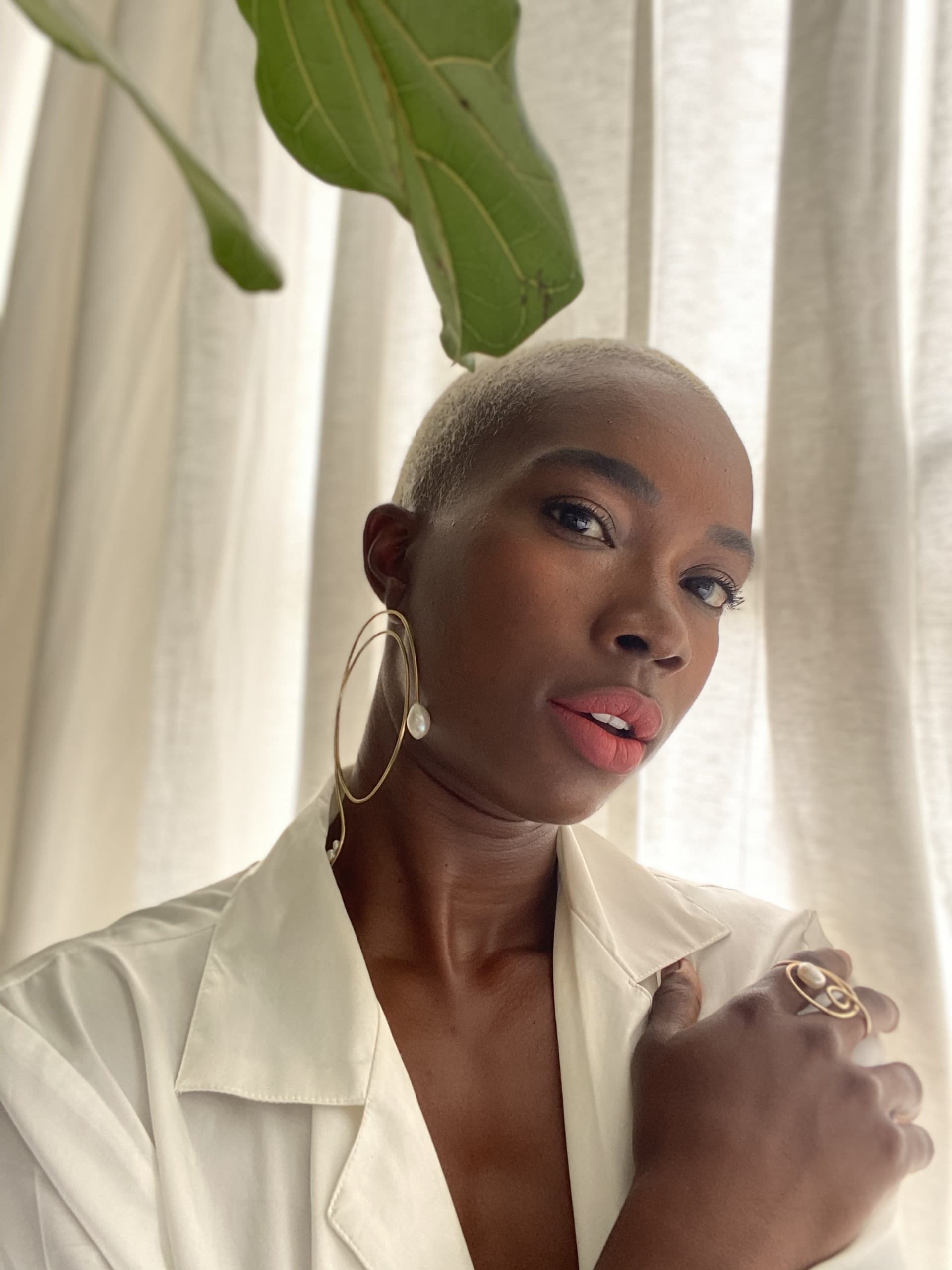 Portrait of Derica Cole Washington wearing a lightweight white shirt and large hoop earrings. The leaves of a plant can be seen dangling in the top portion of the photo.