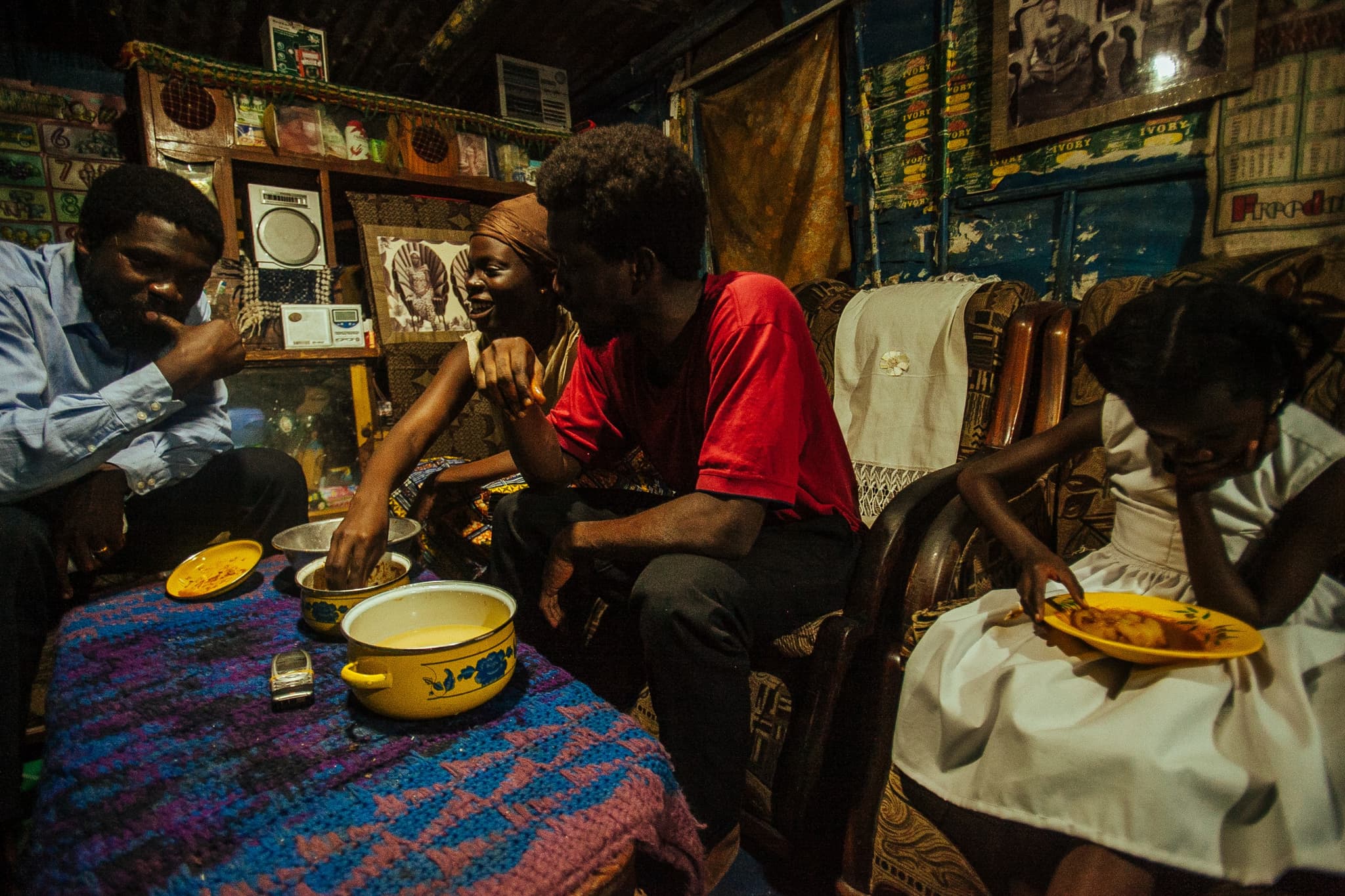 Still from the film "The Burial of Kojo" shows three men sitting around a low table to share a meal. They reach directly into the bowls and ear with their hands.