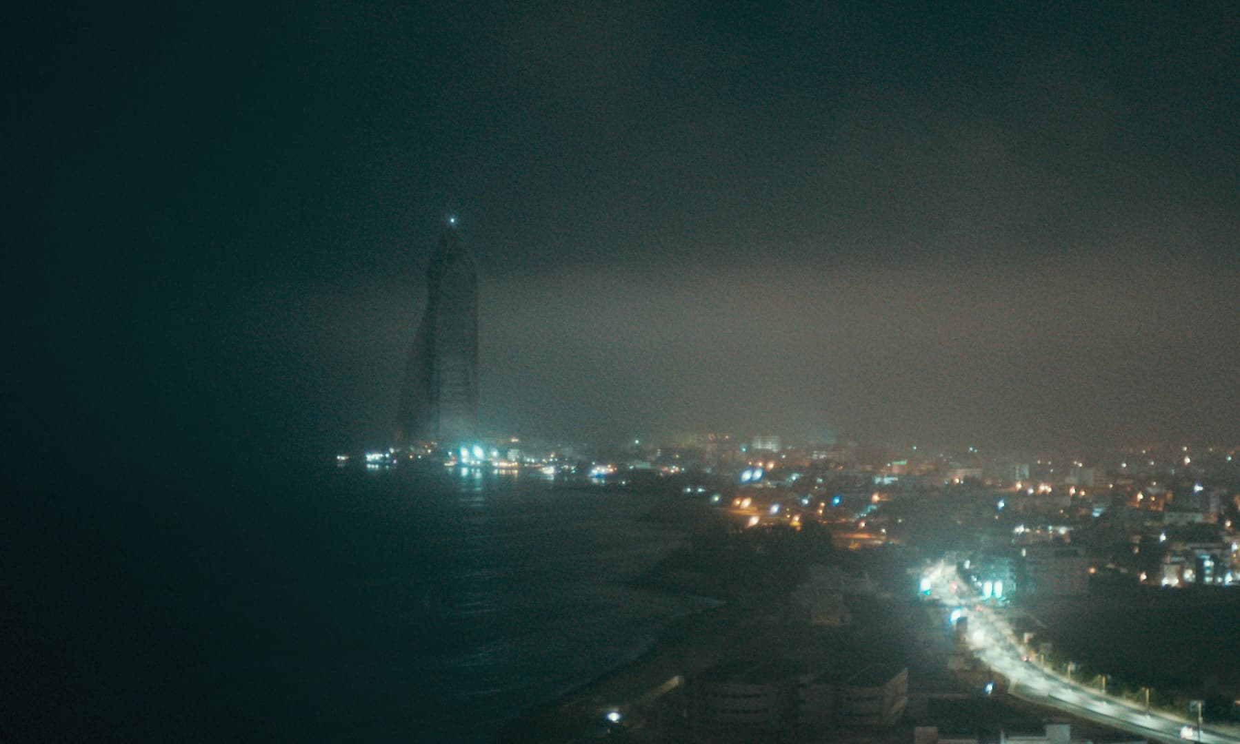 Still from the Film Atlantics shows a dark coastline illuminated by bright city lights.