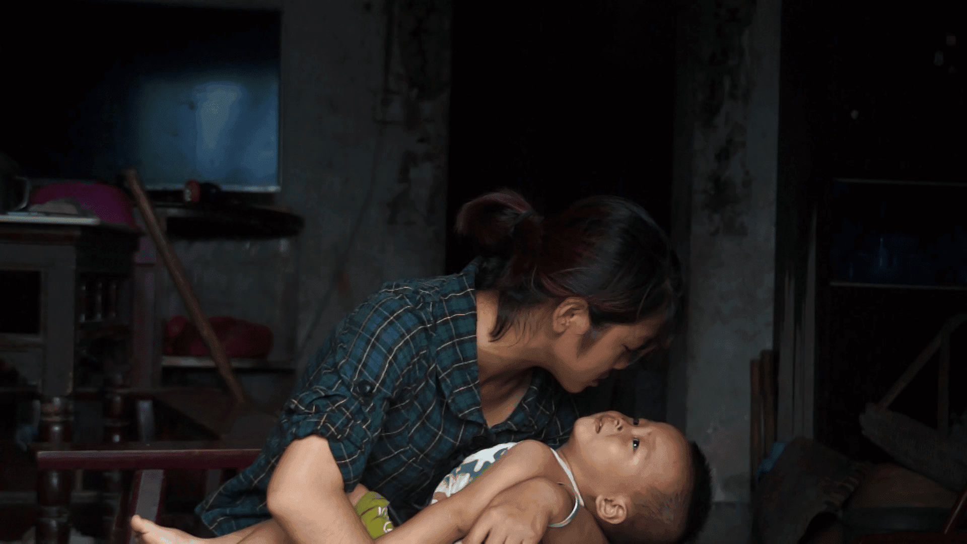 An adult holds a baby in their arms, leaning over them to stare down into their eyes. The baby looks back up at them.