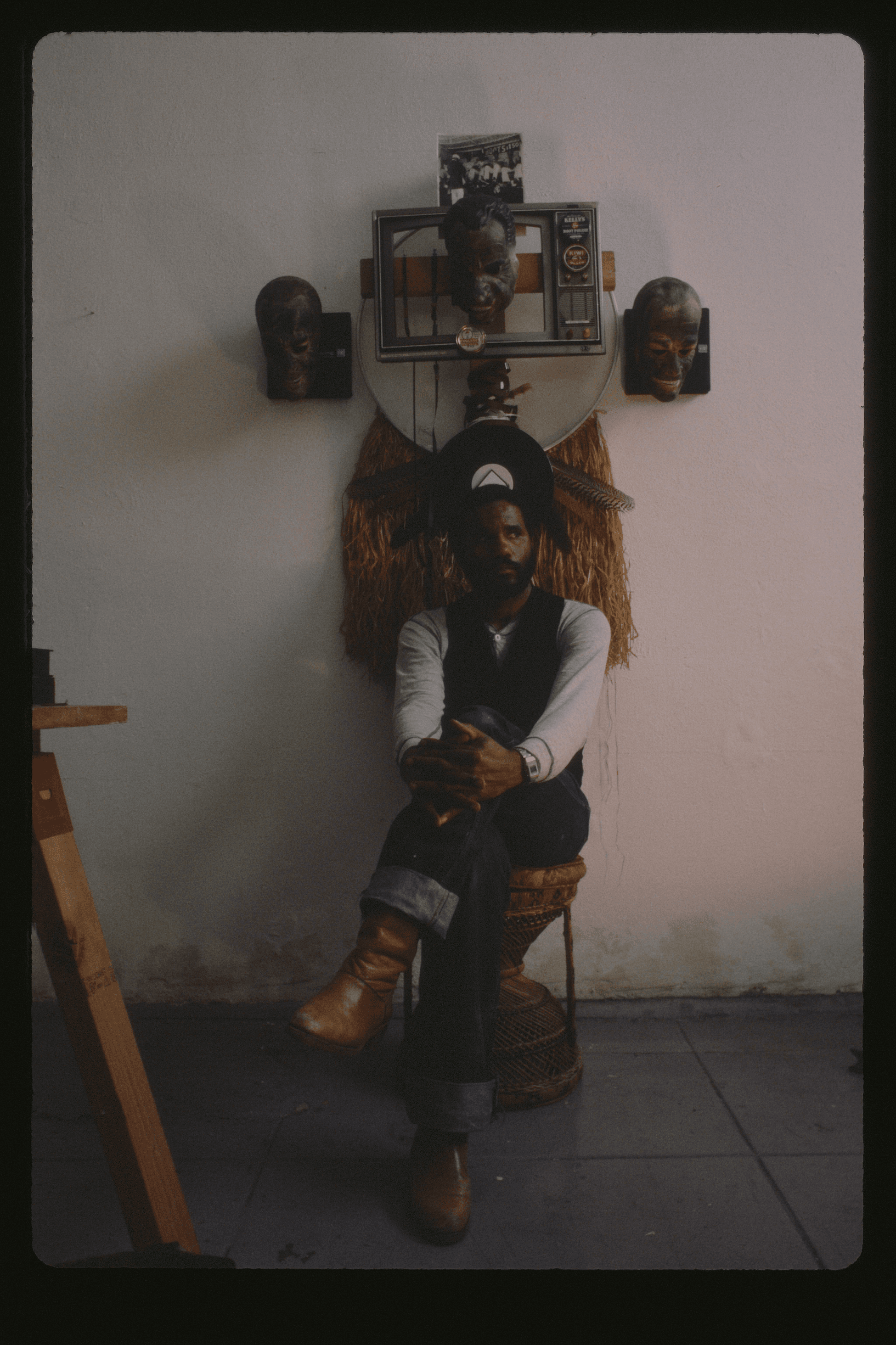 Ulysses Jenkins in studio circa 1983. The artist sits with their legs crossed in front of a complex piece of work.