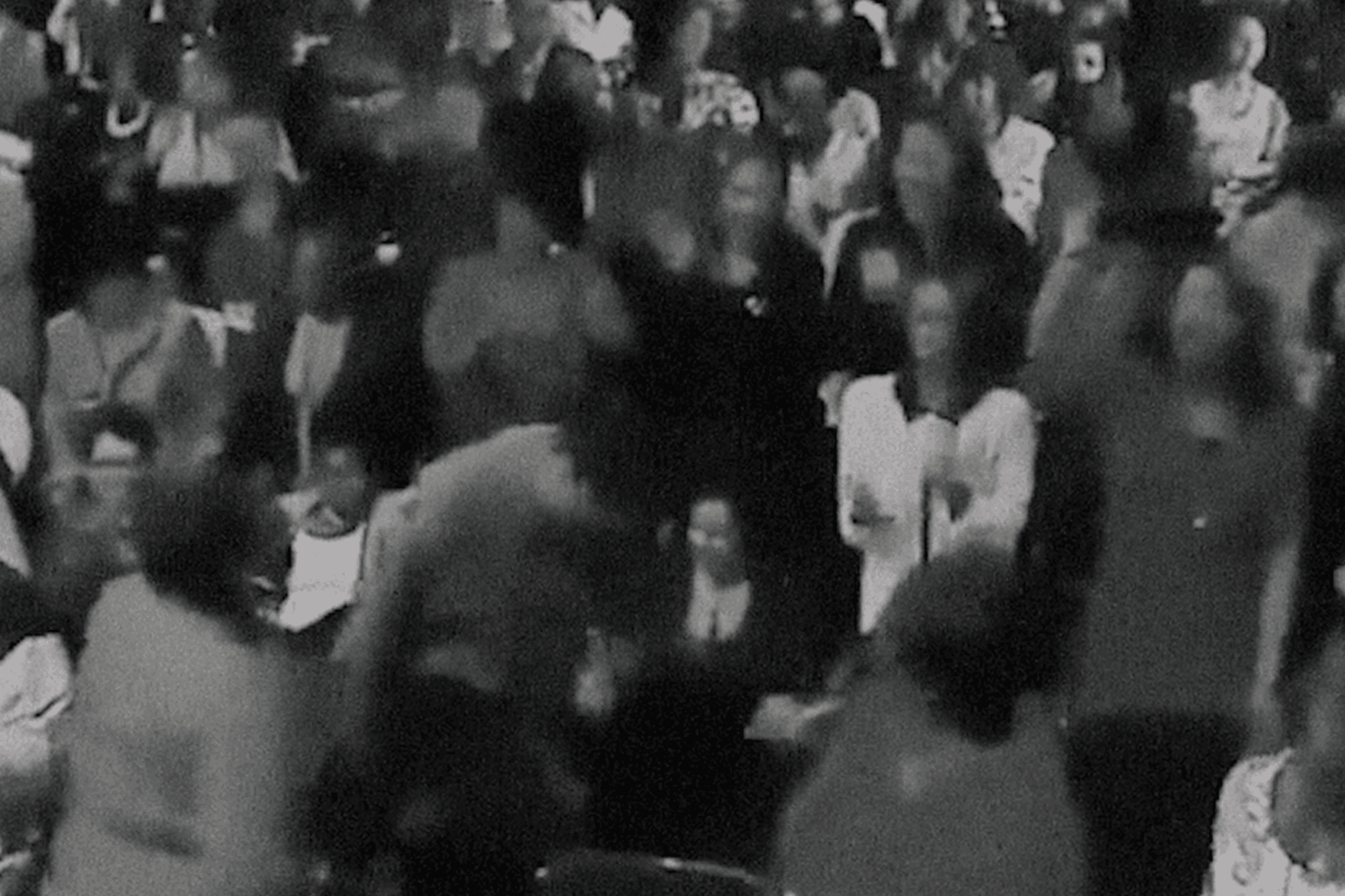 A visual from Revival! The visual looks like a still from an old black-and-white movie. It shows a crowd of people dressed formally, their faces are blurred.