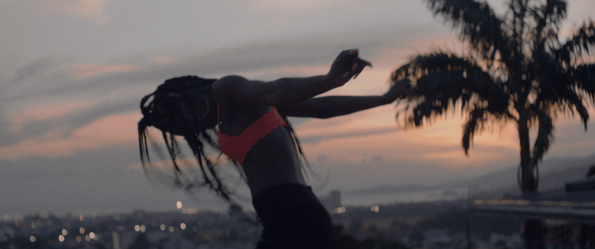 A Black person dances in ecstasy against a backdrop of a setting sun and a palm tree.
