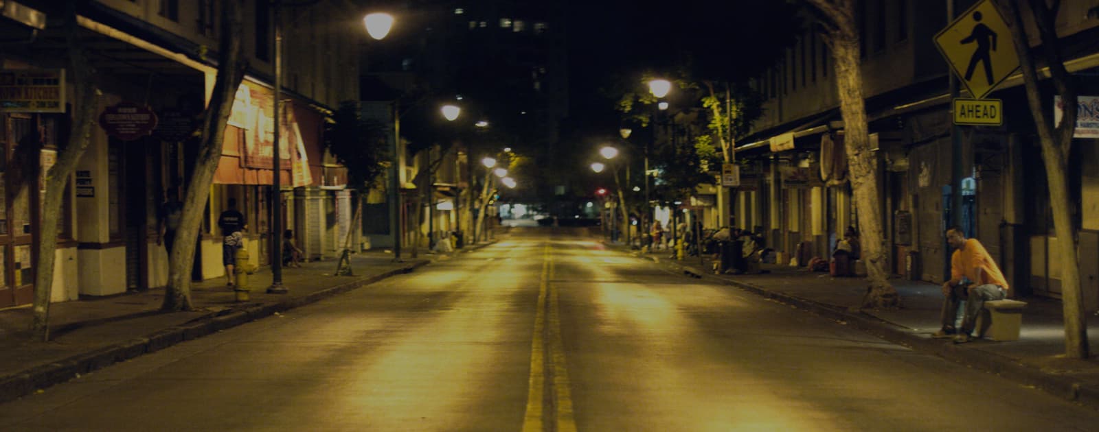 An empty road in Honolulu at nighttime, lit up by street lights.