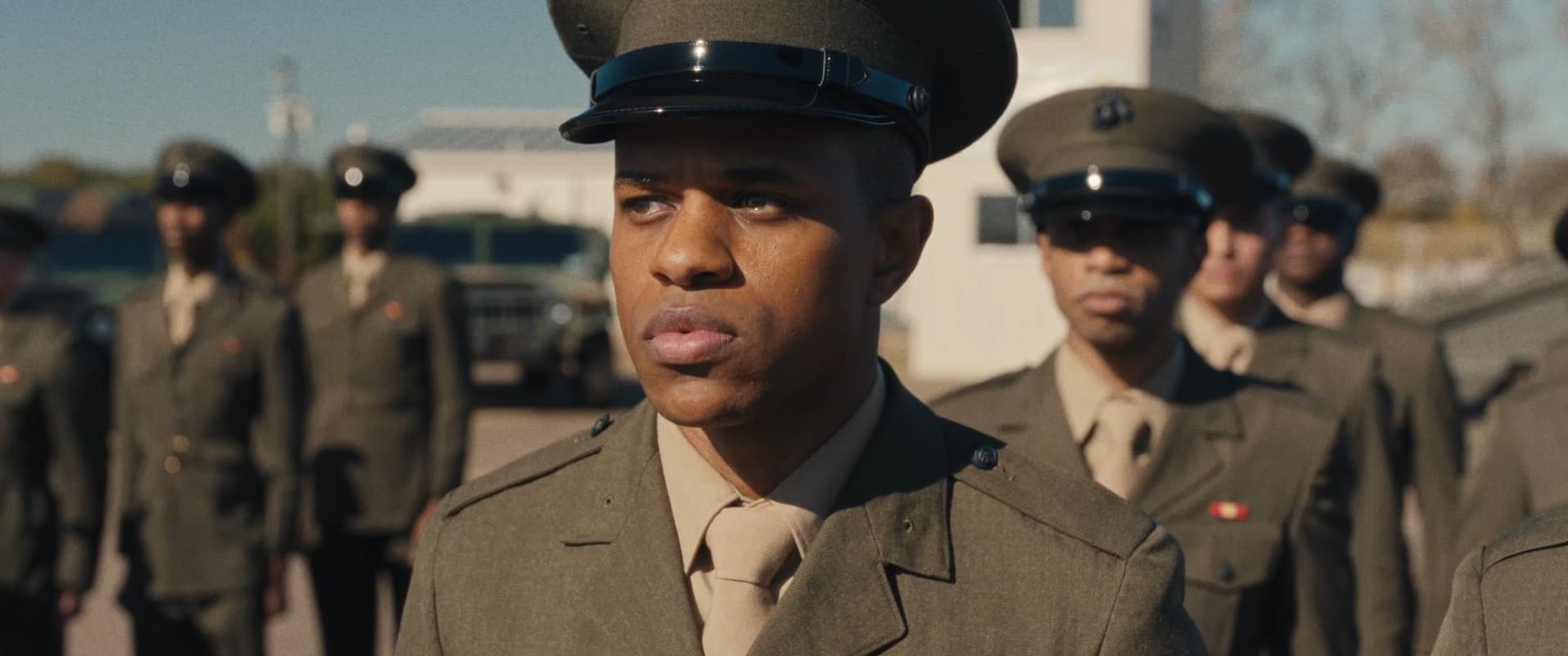 A still from The Inspection shows a Black man looking concerned, pensively at something off screen while standing in uniform in line with other military members.