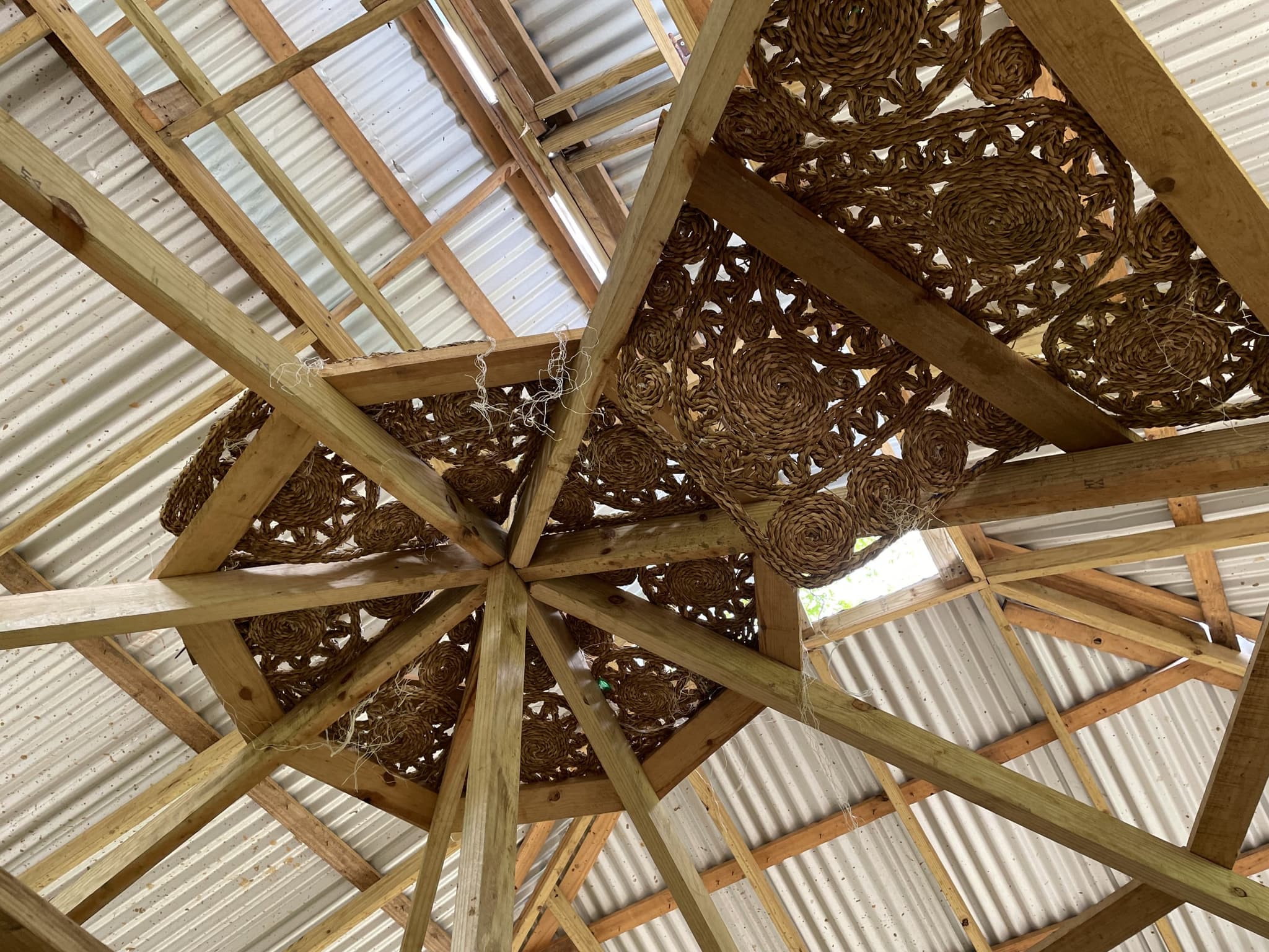 A wooden sculpture piece by Deborah Anzinger hanging from a high wood-beamed ceiling.