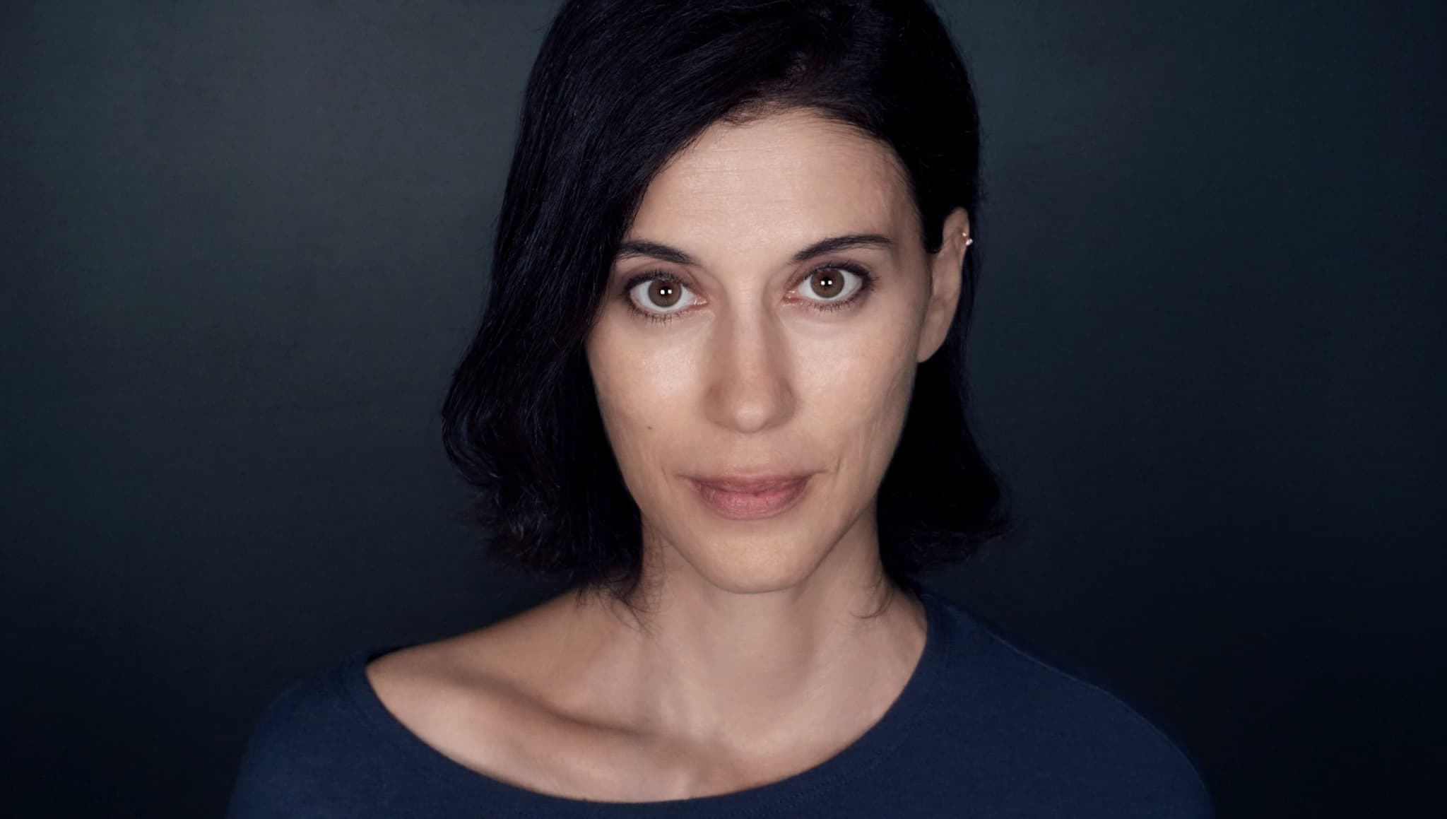 A headshot photo of Cherien Dabis. She is a Palestinian woman, she has long black hair, it is pared to the side, and is looking directly at the camera.