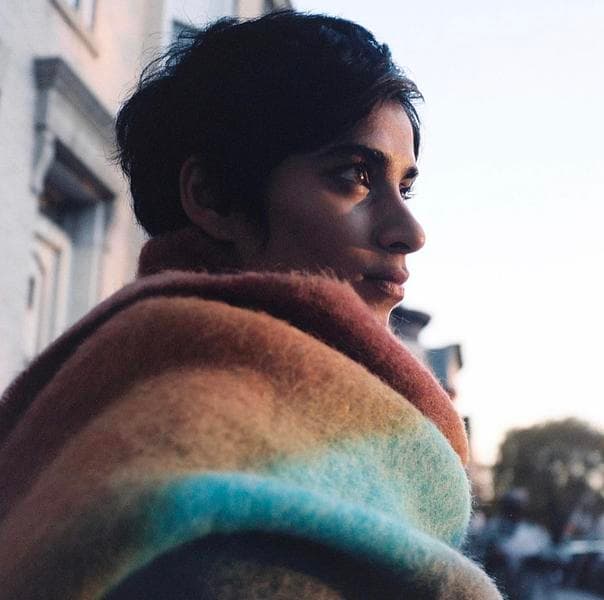 A headshot of Fahira Roisin. She is Bangladeshi. She has short black hair. She has a large colorful blanket wrapped around her. She is looking into the distance.