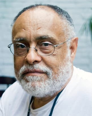 A headshot of Haile Gerima, who wears glasses and a white tshirt