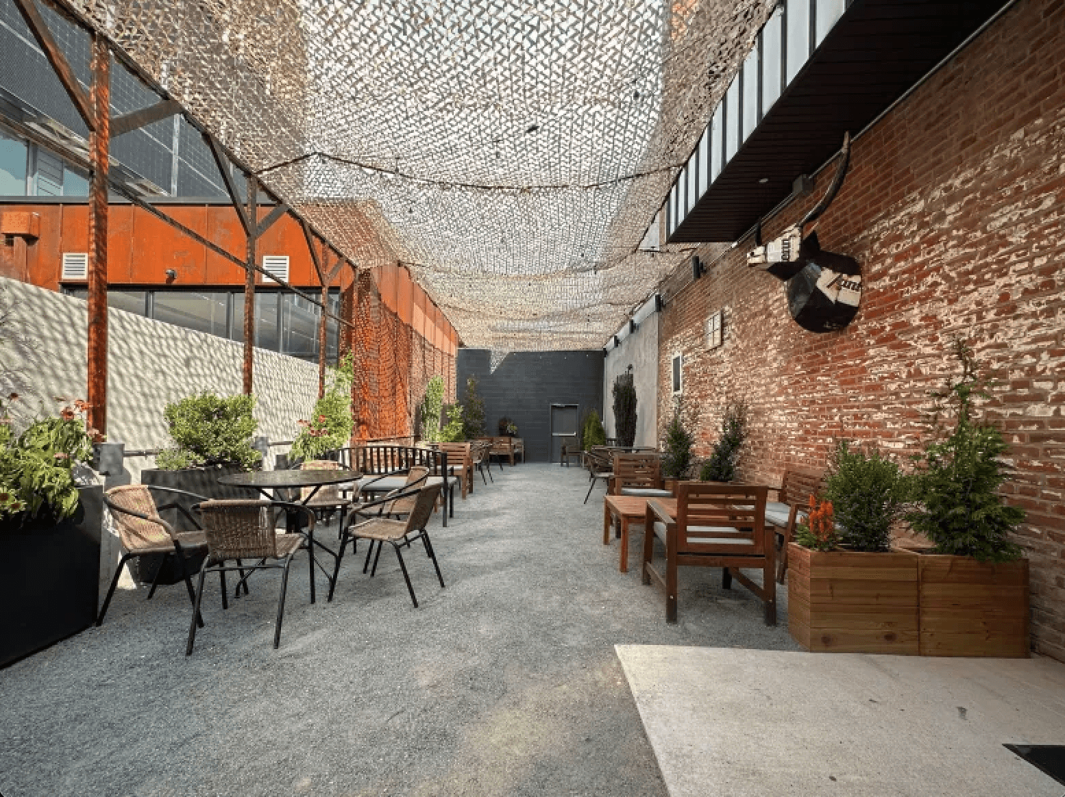 A photo of the outdoor lounge area of Star|Bolt. The area is enclosed by a brick and cement walls with a net hanging above for shade and furnished with patio furniture.