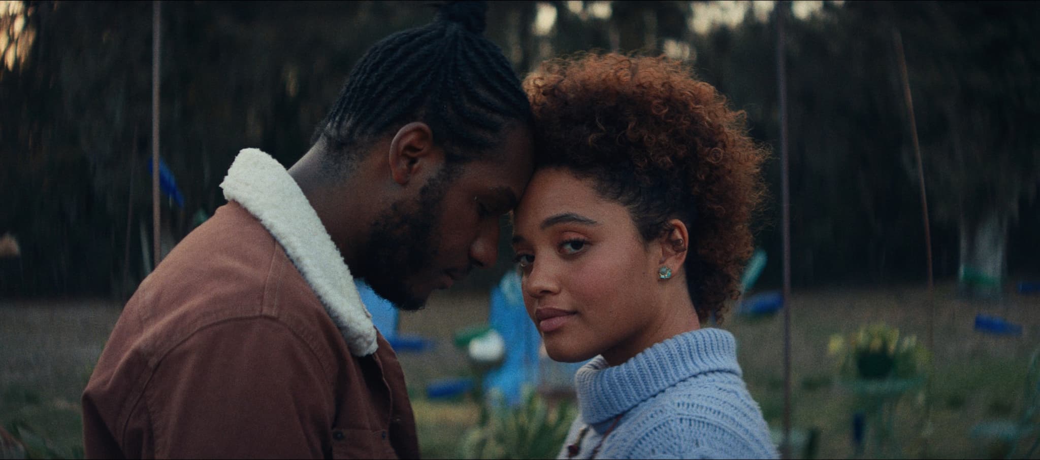A color image from the movie, The Young Wife, with Kiersey Clemeons. A young woman stands next to a man who holds his face to hers. His eyes are closed and her eyes are open, staring at the camera.