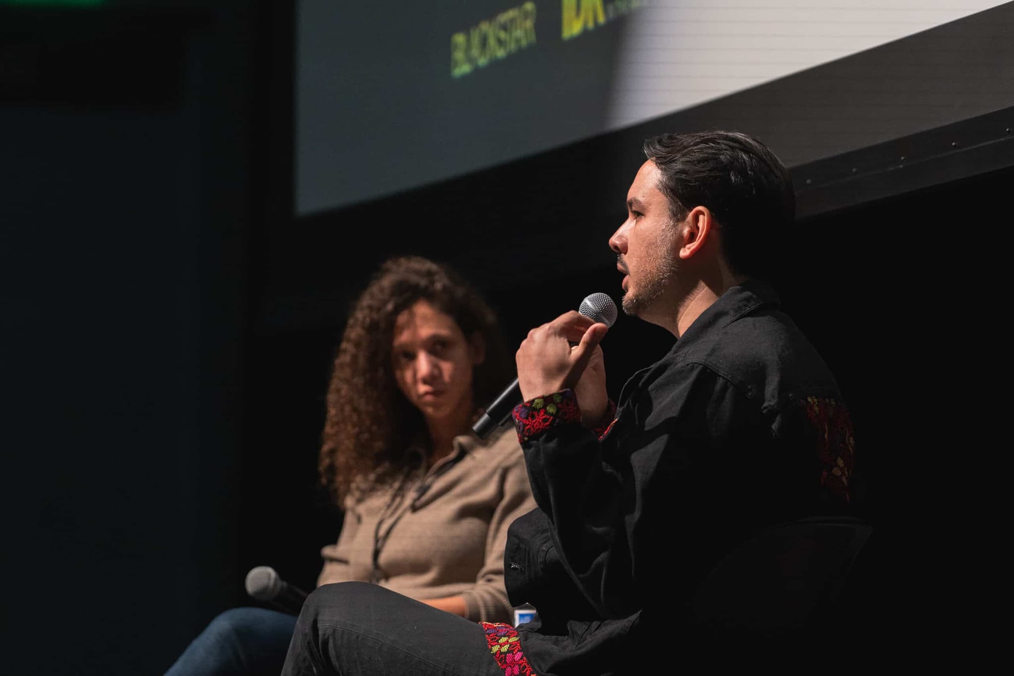 A photo of Suneil Sanzgiri in conversation with someone. They are on stage, both people are holding microphones.