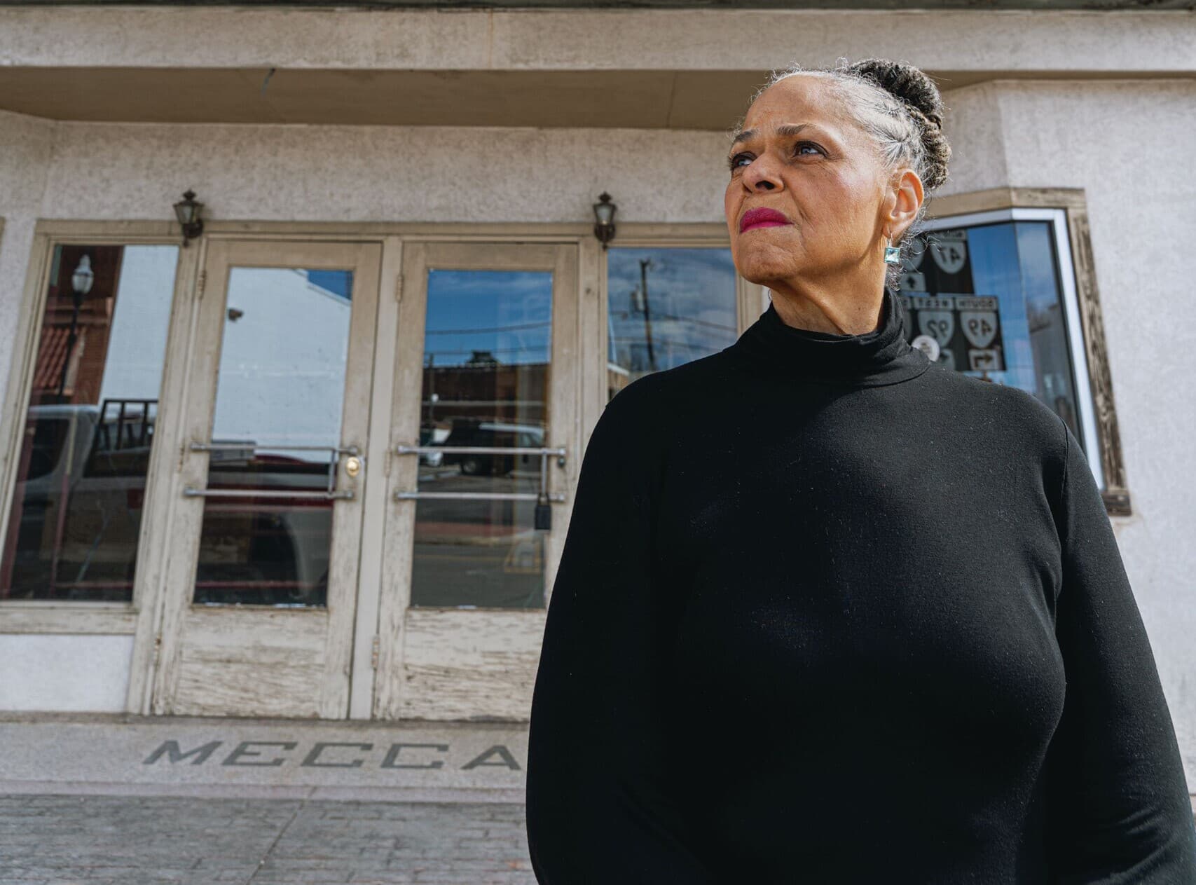 Beverly Wood is standing in front of the Mecca Theatre in Chase City and looks off to the left.