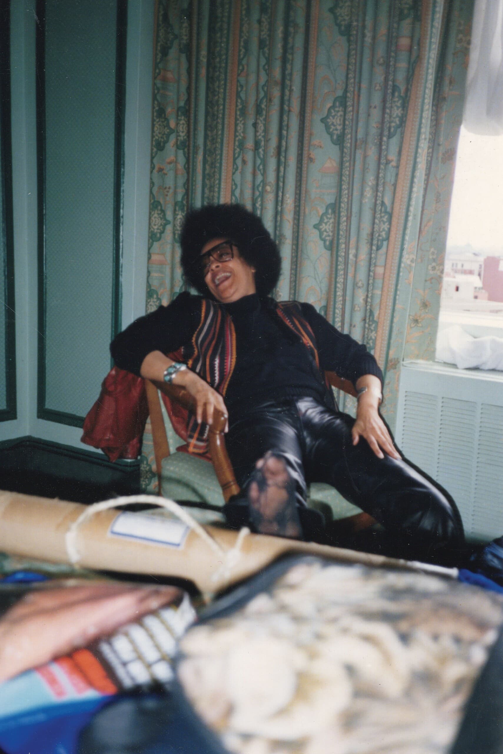 Toni Cade Bambara is sitting on a chair and laughing, looking to the left.