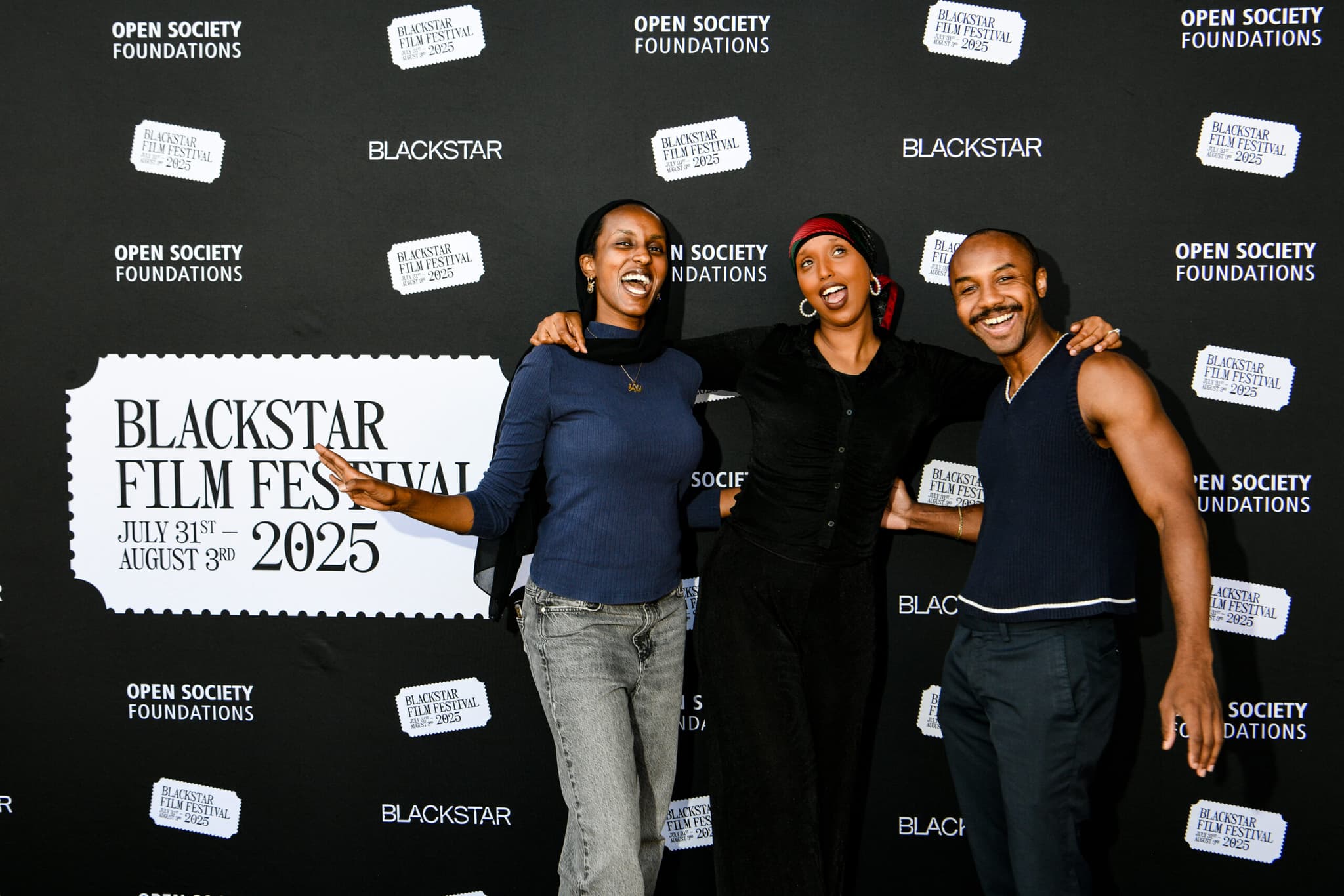 A photo of three people posed in front of the step-and-repeat at BlackStar Film Festival. They are smiling and laughing.