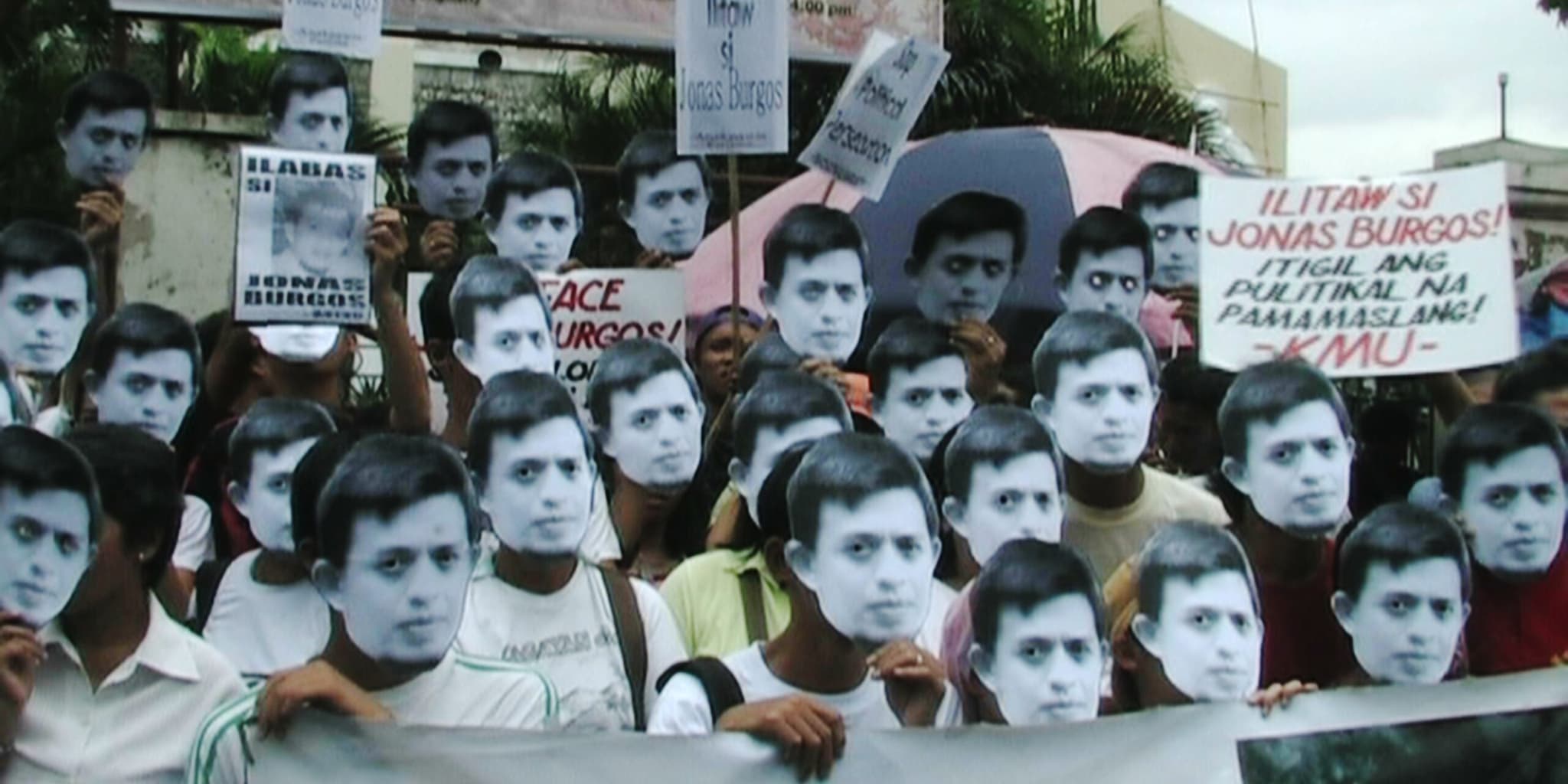 Protesters wearing identical paper face masks hold signs in Tagalog and English demanding the surfacing of Jonas Burgos