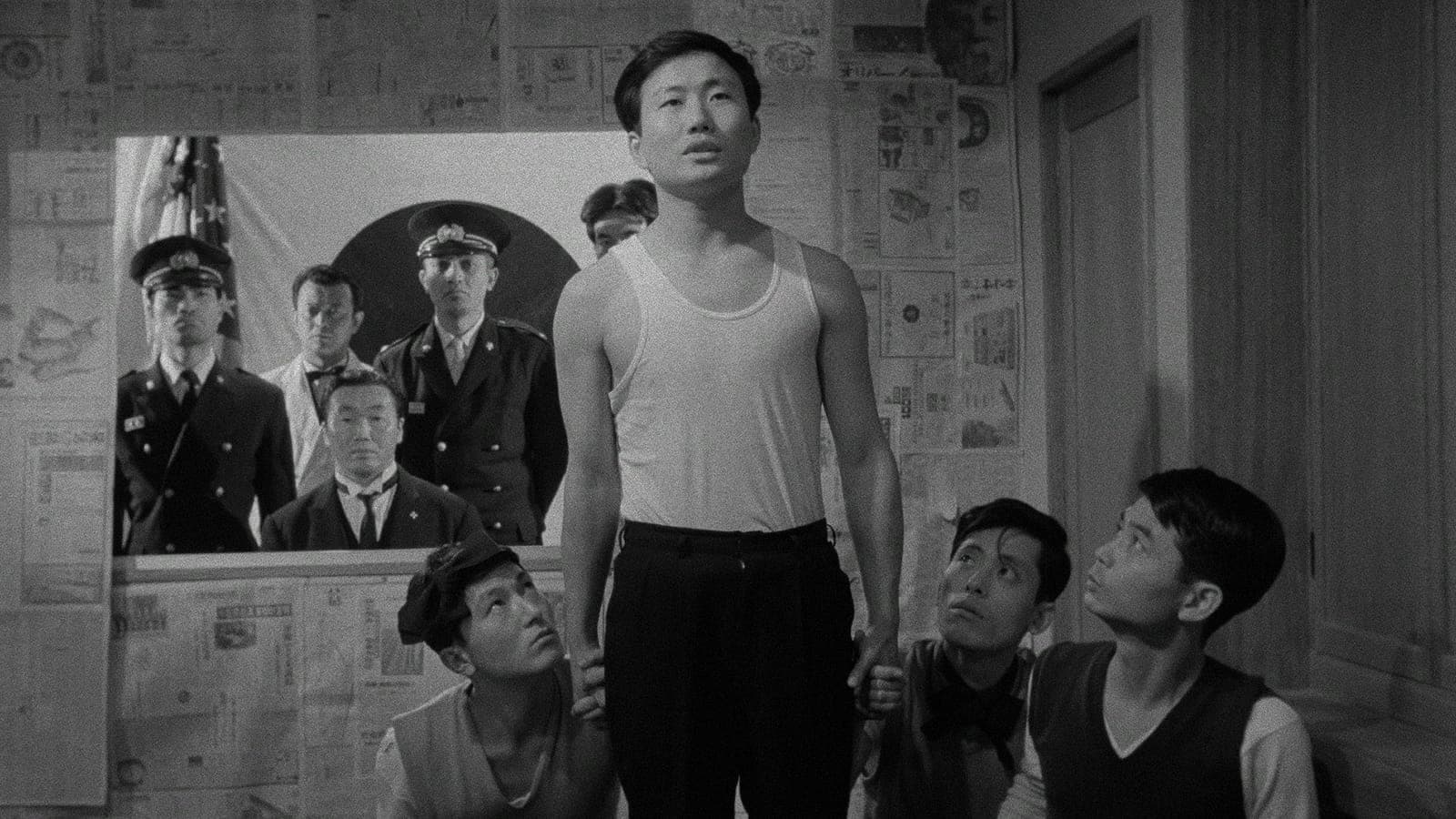 A man in a white shirt stands between three men who are kneeling around him.