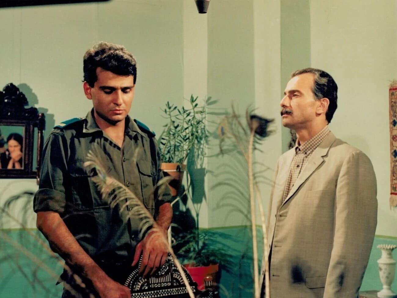 A still from Return to Haifa shows two man standing together. The younger man is in military fatigues and is looking down. The older man looks at him.