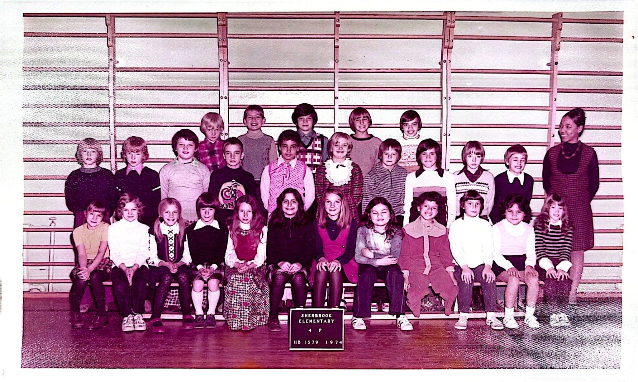 A traditional school class portrait of students posing alongside their smiling teacher.