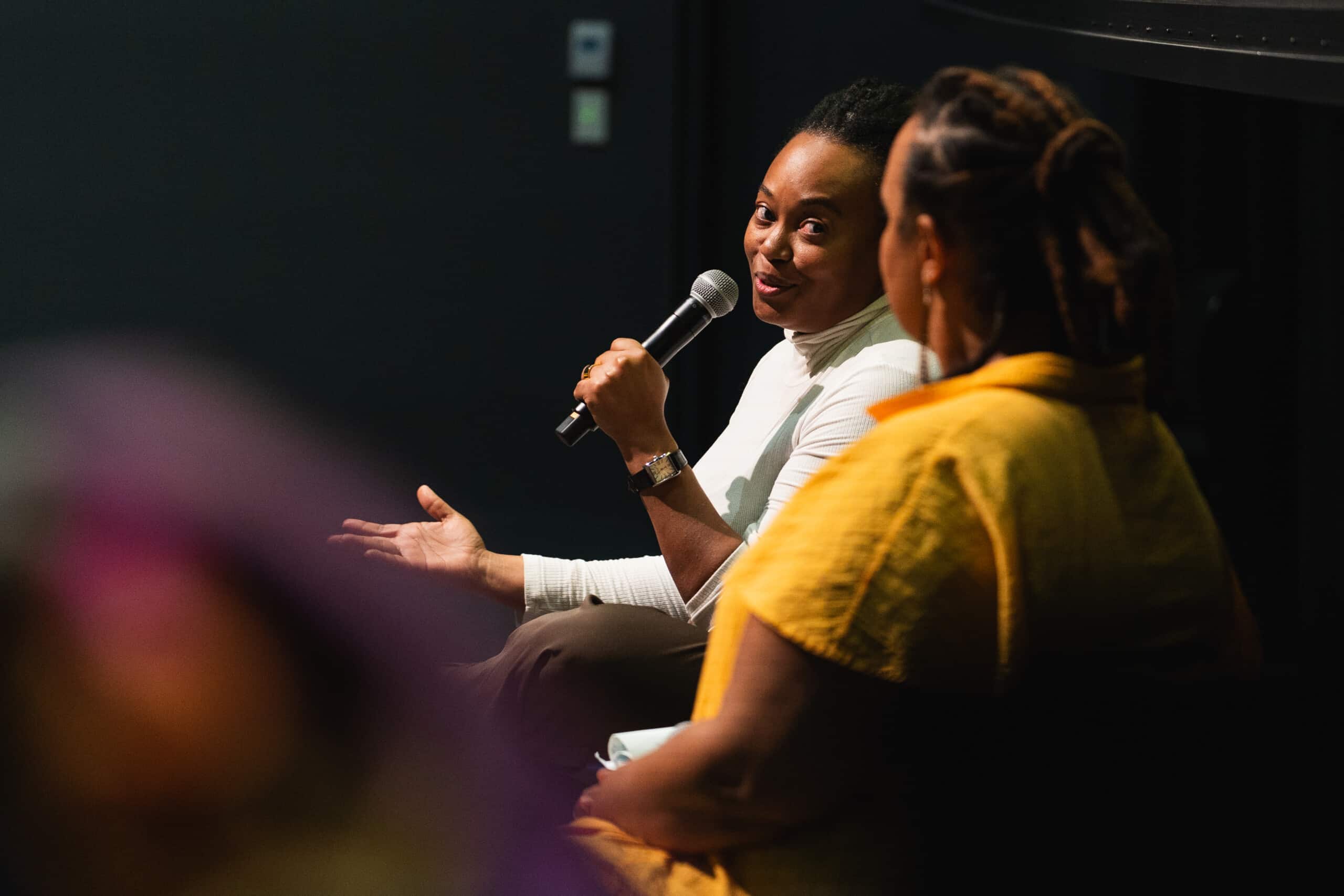 A photo of two people on stage at the 2025 William and Louise Greaves Filmmaker Seminar. One person is holding a microphone.