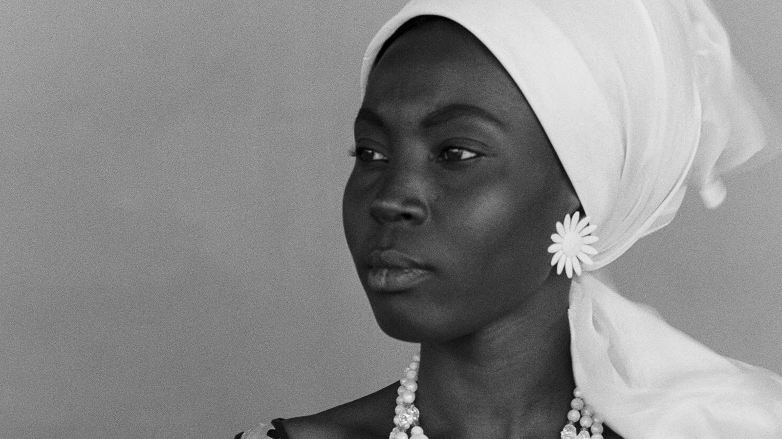 A close-up photo of a young Black woman looking into the distance. She is wearing a white head scarf.