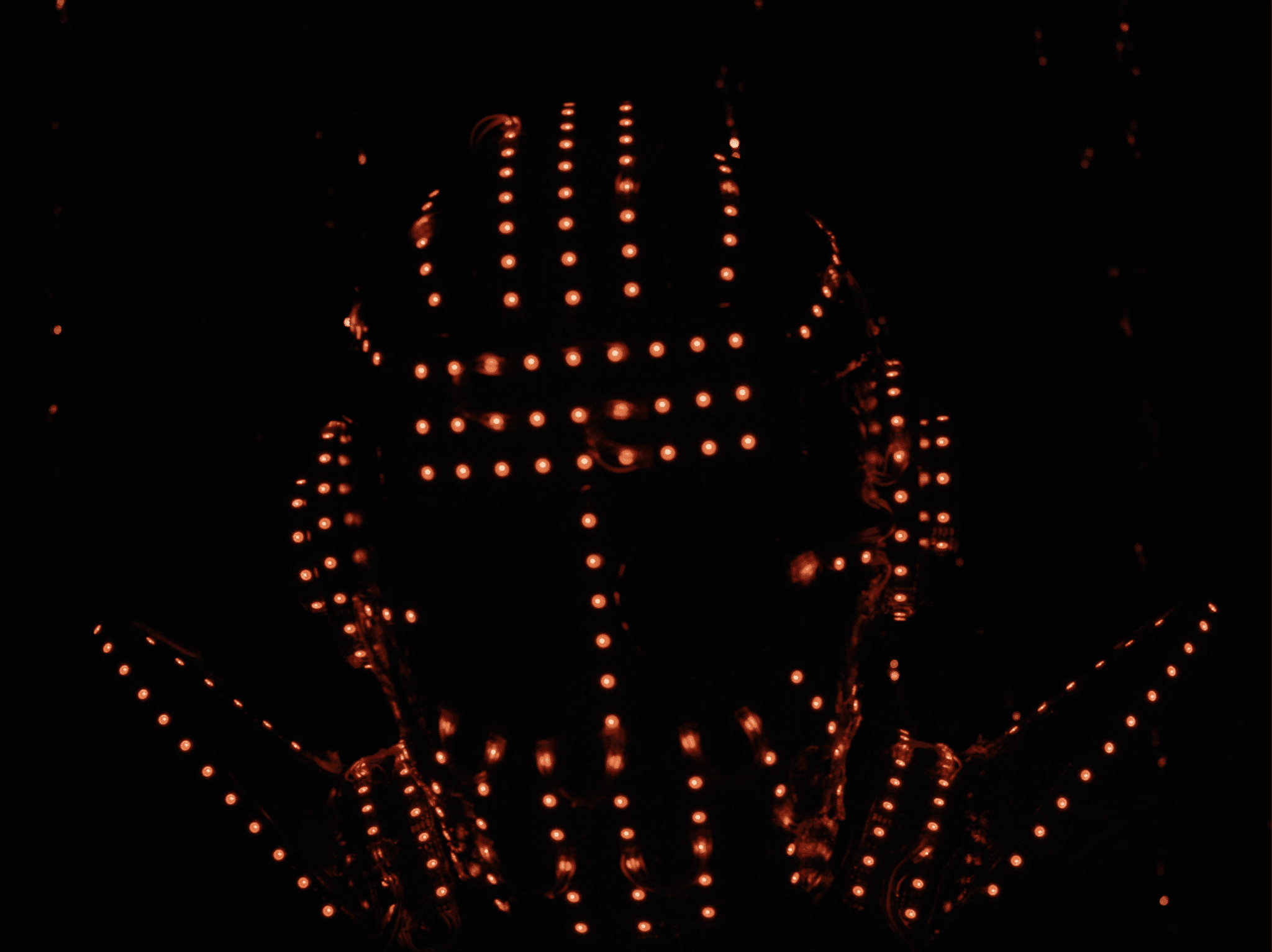 Still from the film "T" shows a "soundsuit," an intricate collection of lights arranged to take the shape of a human body. In this image, the shape of a head can be seen in the dozens of orange lights.