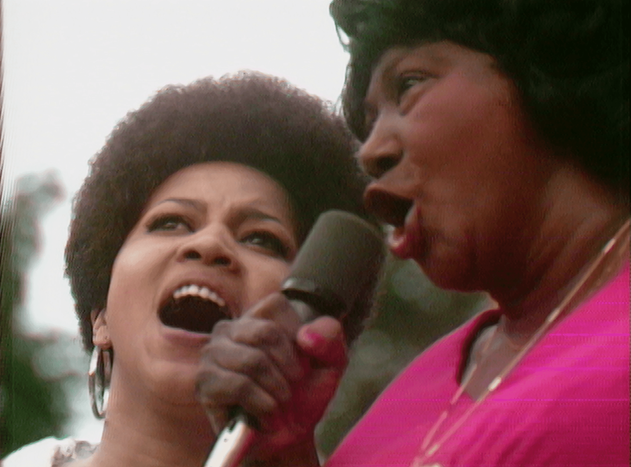 Still from the film "Summer of Soul" is a close-up image of two Black women singing into a microphone.