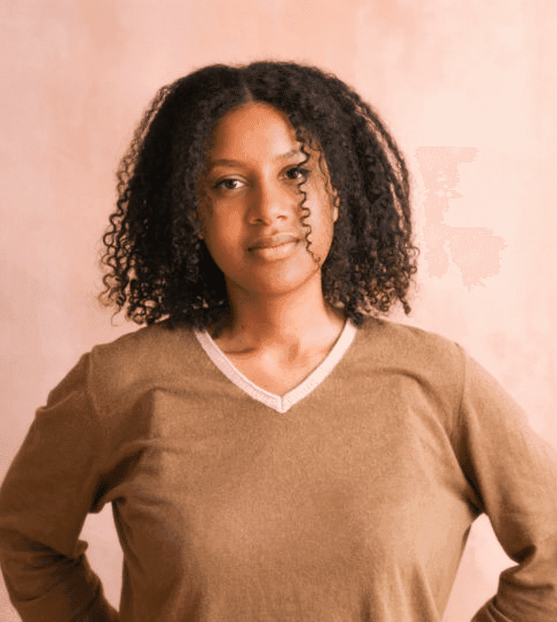 A headshot of Mariam Dembele. She is a Black woman with shoulder length curly black hair. She is wearing a tan sweater and is looking at the camera with a soft expression.