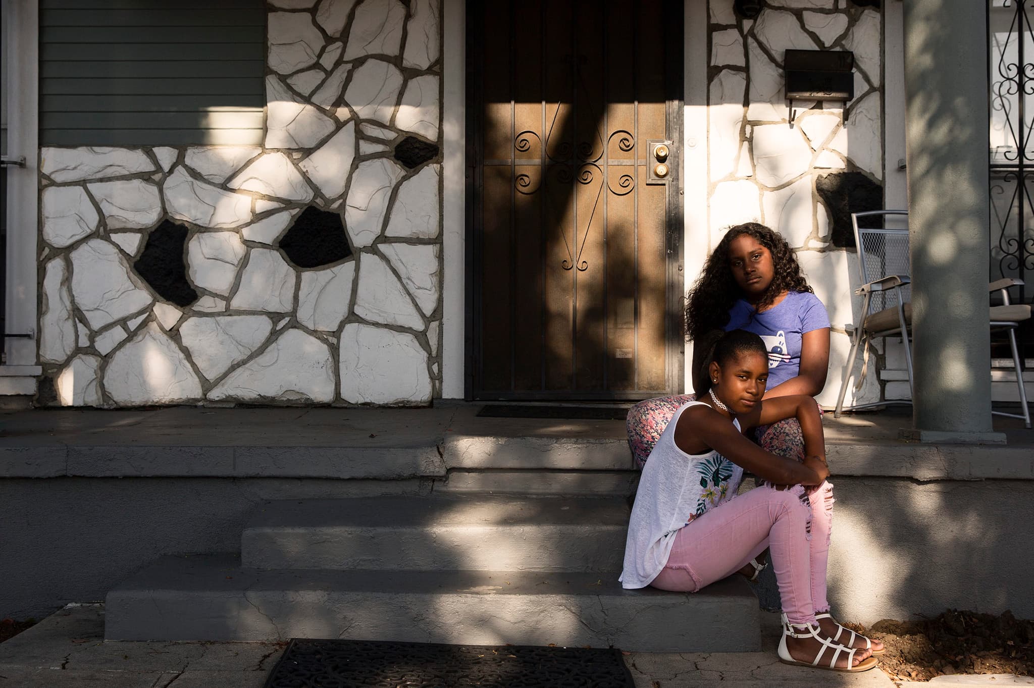 A still from A Love Song for Latasha shows two young girls sitting on the steps of a house in Los Angeles.
