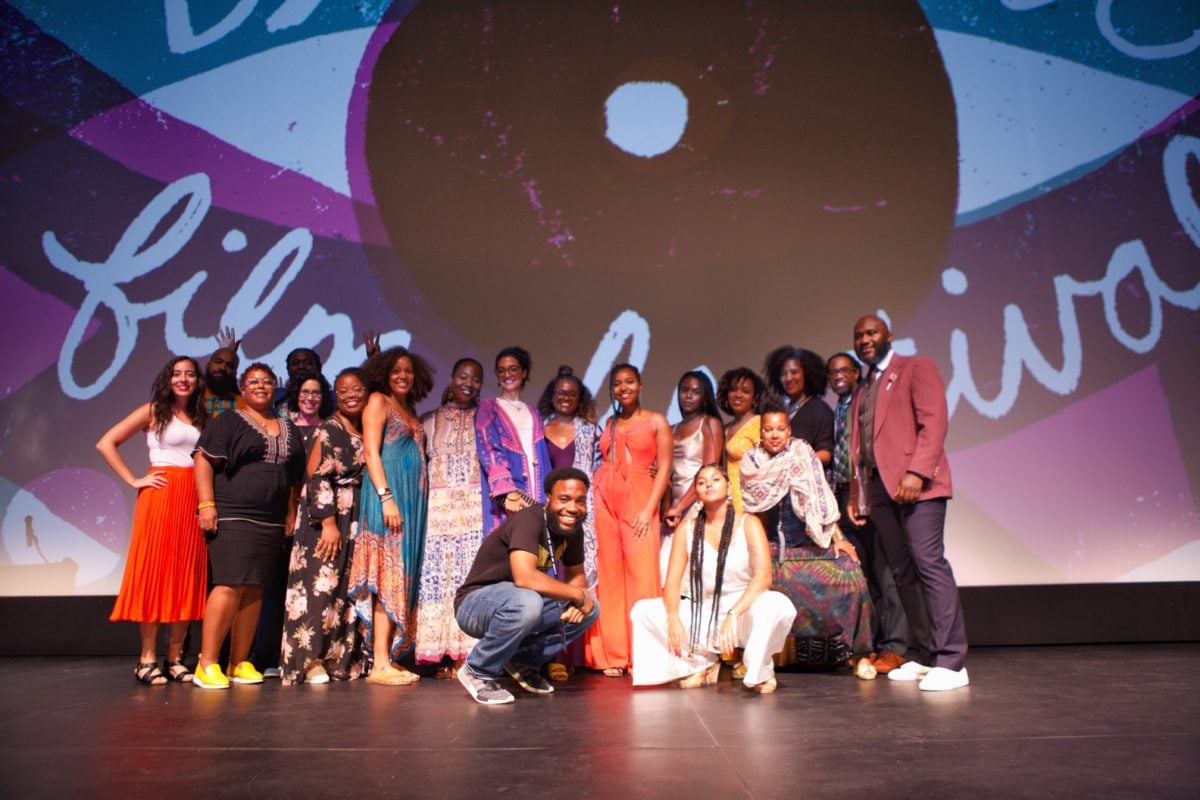 A group photo of BlackStar Project's staff. They are standing on a stage in front of a screen with the BlackStar graphic on it. The staff is smiling.