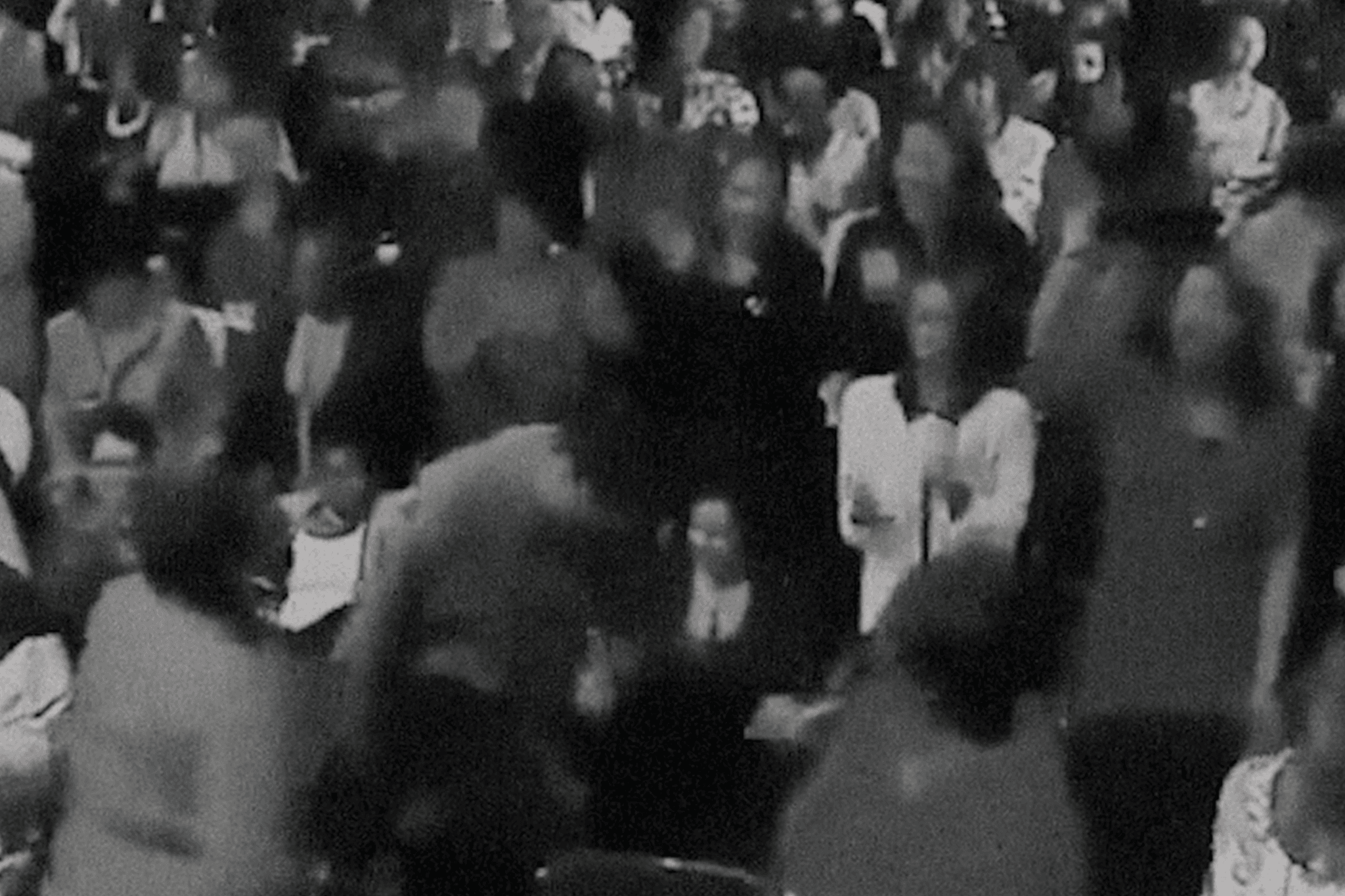 A visual from Revival! The visual looks like a still from an old black-and-white movie. It shows a crowd of people dressed formally, their faces are blurred.