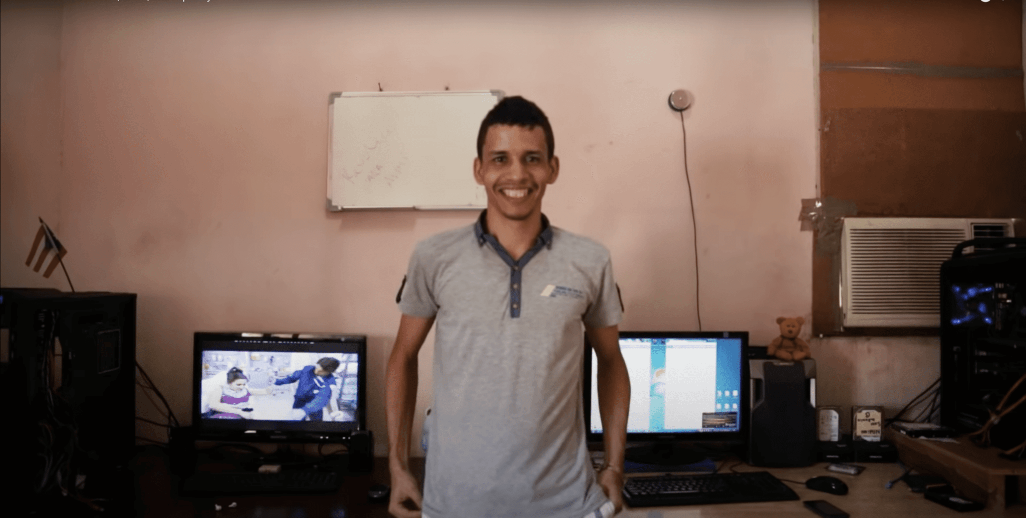 Still from the video report "This is Cuba's Netflix, Hulu, and Spotify — all without the internet," by Johnny Harris. Shows a Cuban person standing in front of multiple laptop and computer screens on a table.