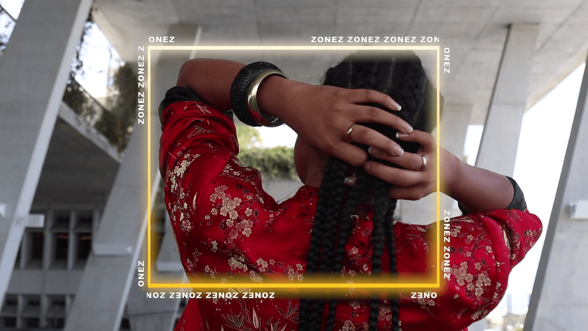 A Black person is filmed from behind, holding their hair in both their hands.