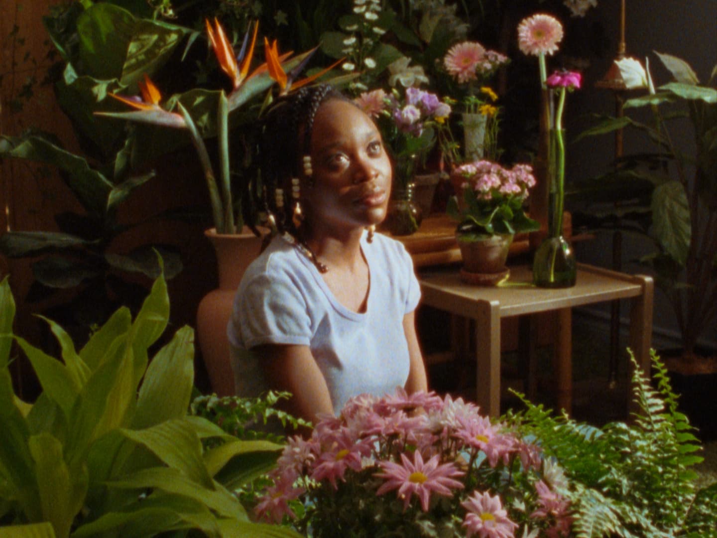A still from CETTE MAISON, featuring a Black person sitting amongst flowers and greenery, inside.