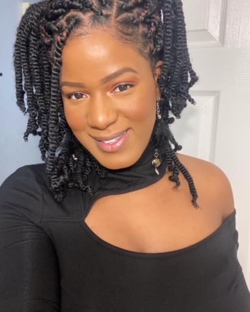 Photo of Antoinette Stewart shows her wearing an asymmetrical black top and long dangling earrings. Her short twisted hair is arranged in a half-up/half-down style.