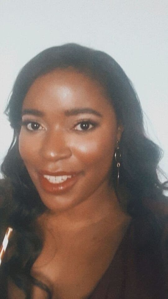 Headshot of Isabel Rieser shows her with long black curly hair. She wears gold hoop earrings and smiles as she looks into the camera.