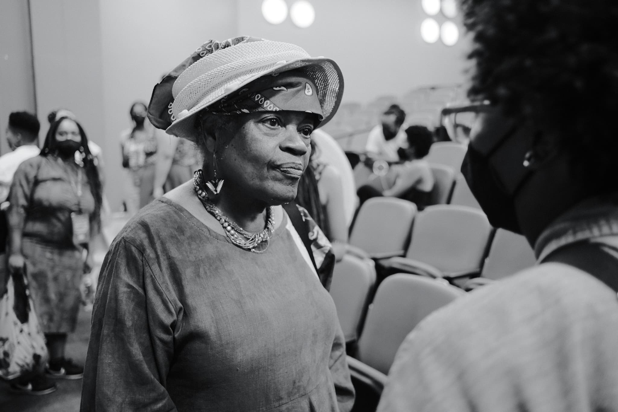 Photo of Dindga McCannon speaking to an audience member, taken by Mochi Robinson, in black and white.