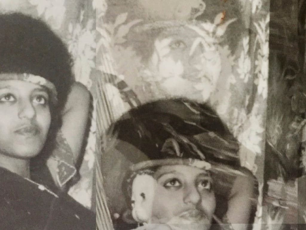 A black-and-white photo, it shows two Ethiopian people looking into the distance. There is a decorative cloth behind them.