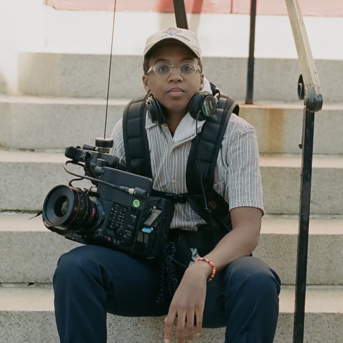 A photograph shows a portrait of Cai Thomas sitting on the steps outside of a building with her camera gear.