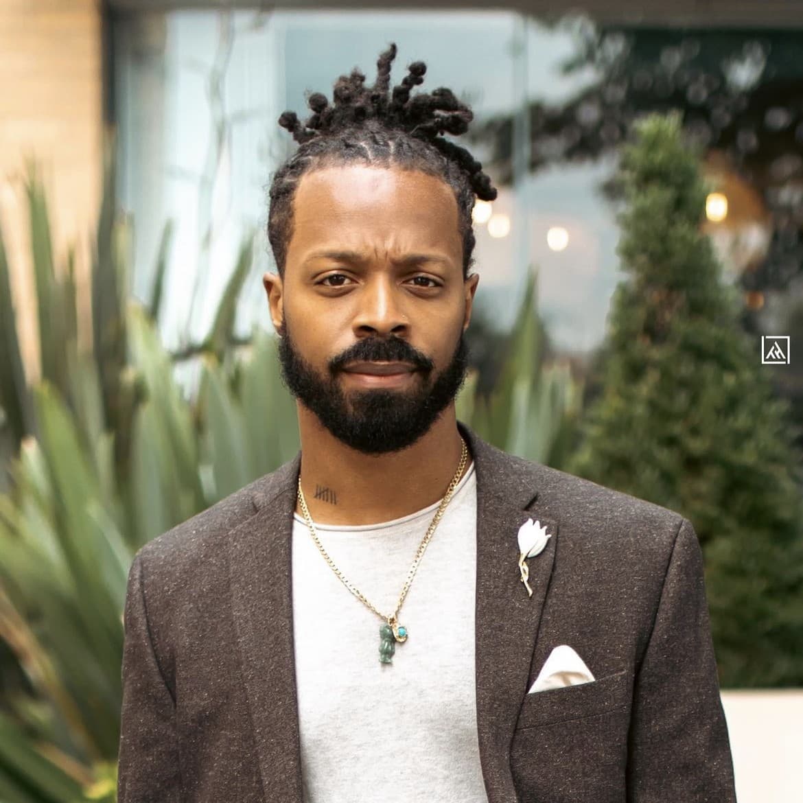 A photograph shows a headshot of Tremain Hamilton outside. There are large green plants in the background in front of a brick building with large glass windows and ambient lighting inside.