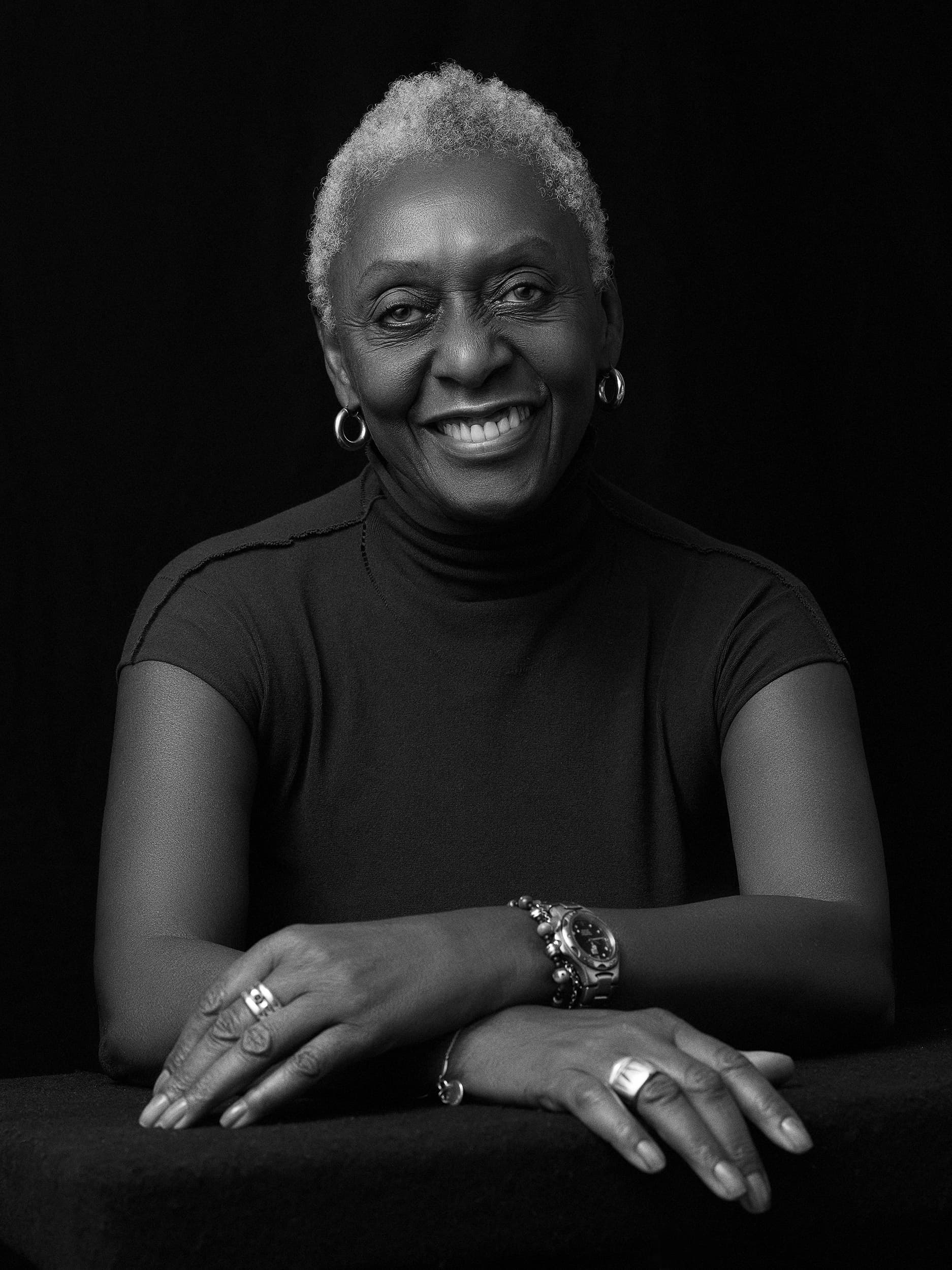 Headshot of Bethann Hardison. Bethann is an older Black woman, she has short gray hair. She is wearing a black turtle neck shirt and hoop earrings. She is smiling.