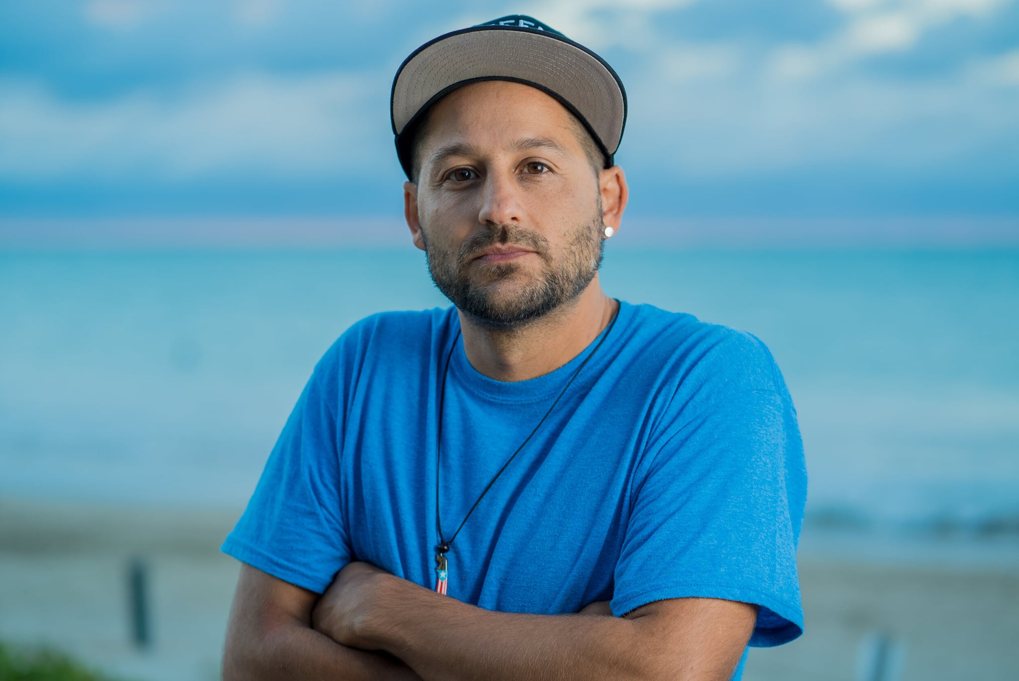 A headshot of Eli Jacobs-Fantauzzi, a Puerto Rican man. He is wearing a blue shirt and a baseball cap.