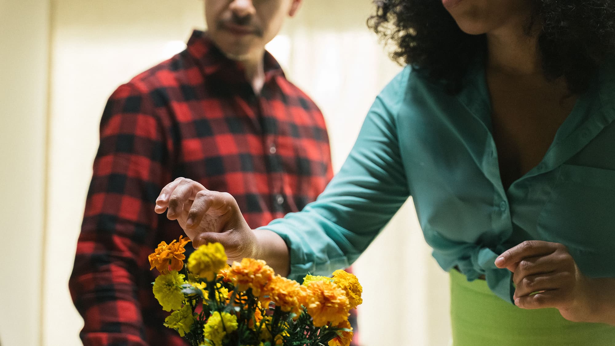 A still from Tonight, We Eat Flowers. It shows the bodies of two people standing behind a vase of flowers. The woman is reaching in to grab one.