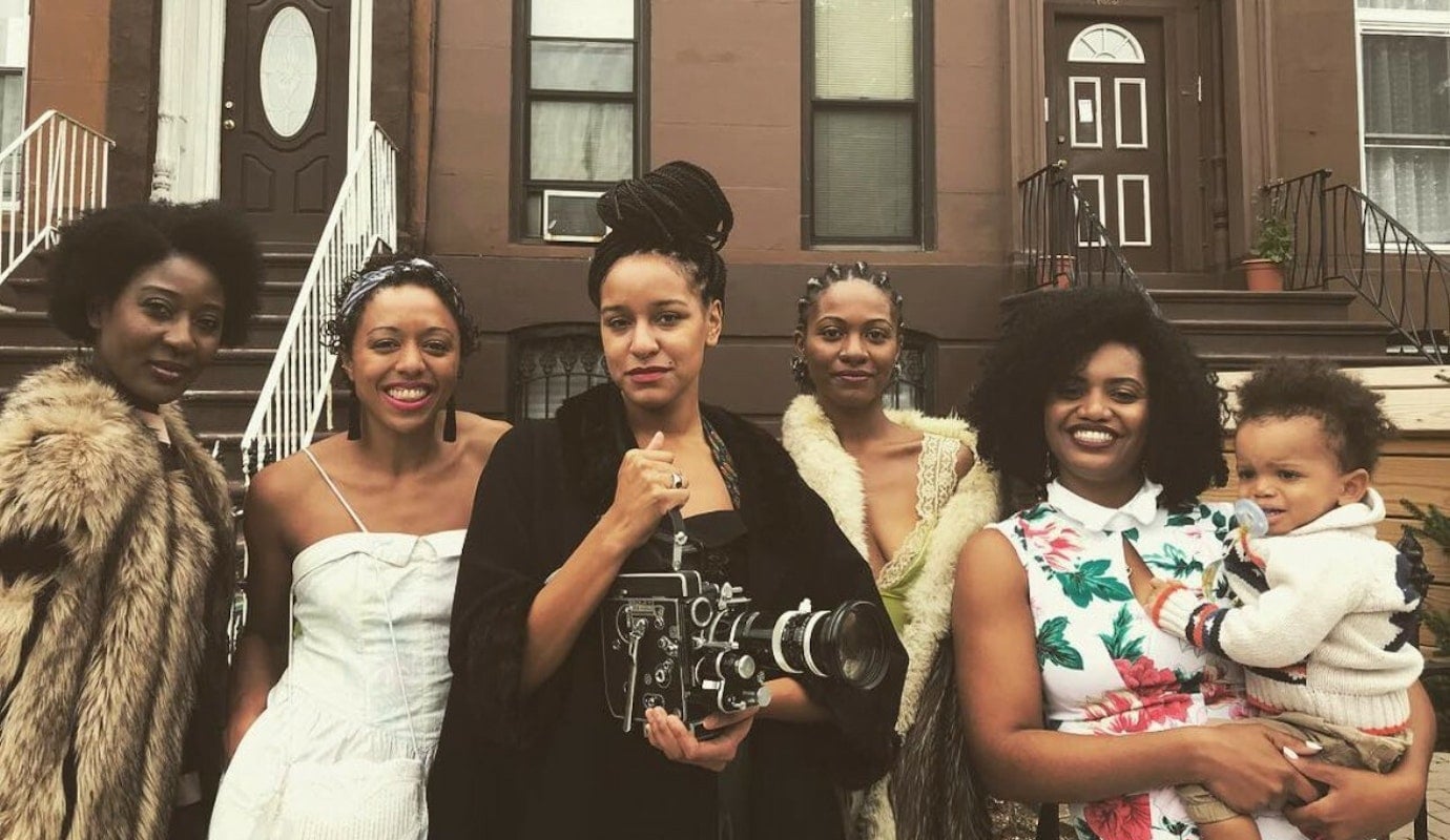A production still from 1800-Lovable shows filmmaker Rebeca Huntt standing with four other women. One is holding a baby. They are smiling.