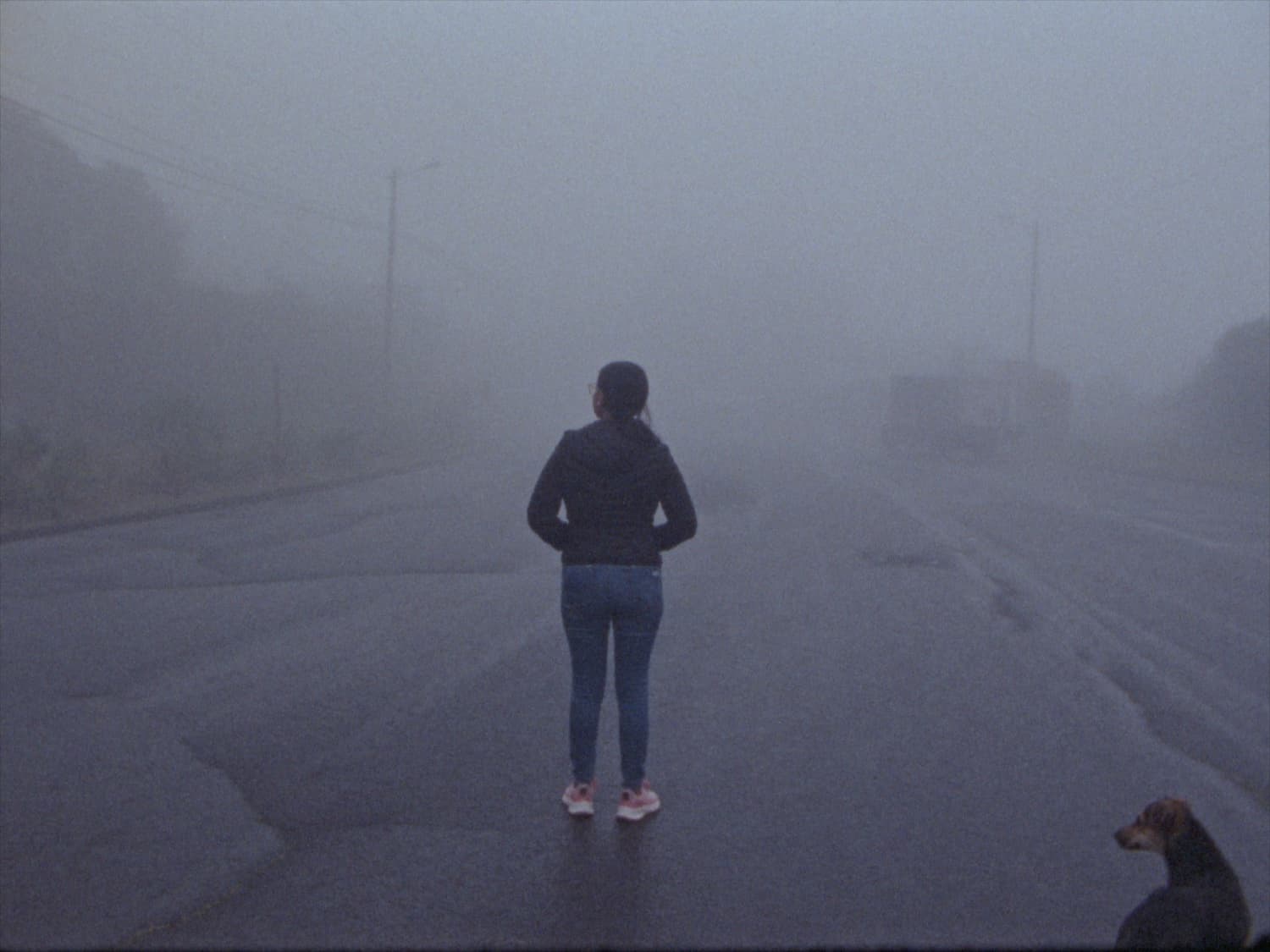 A still from Tonada Menguante shows a woman standing in the middle of a foggy road. Their back is turned to us.