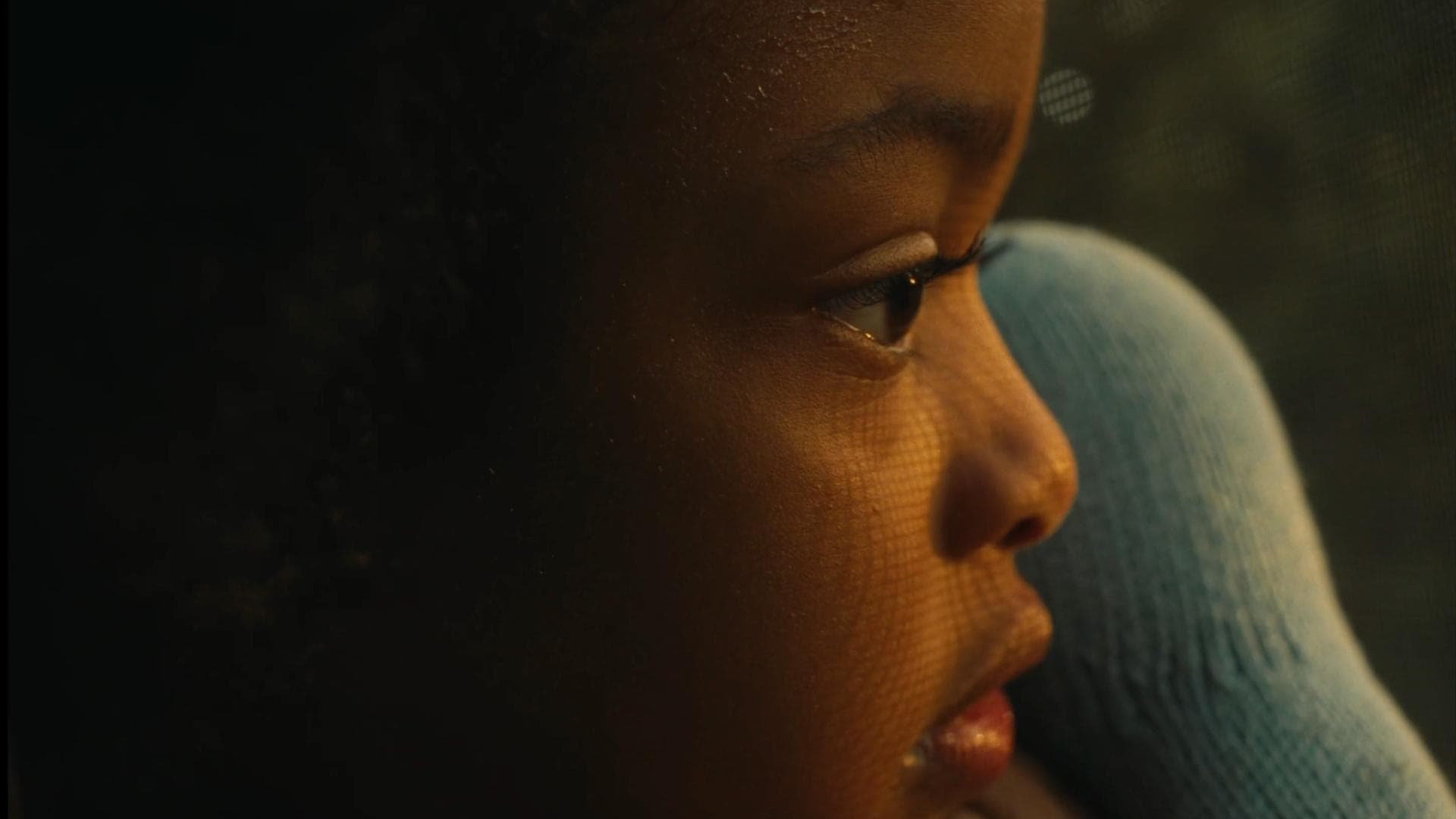 A film still from all the love i could handle shows the side profile of a young Black girl curiously staring at something off screen.
