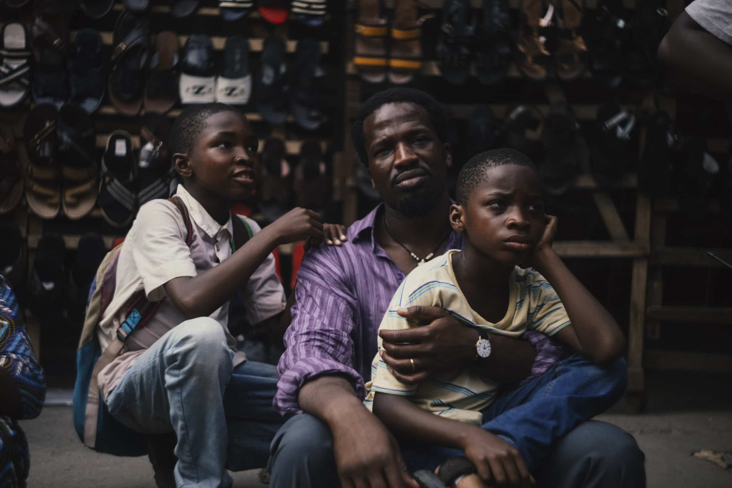 The dad is sitting down, one of his sons sits on his lap with legs crossed, and the other son is crouched down next to them.