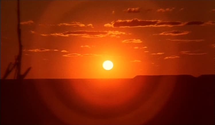 A setting sun in front of a red sky and landscape.