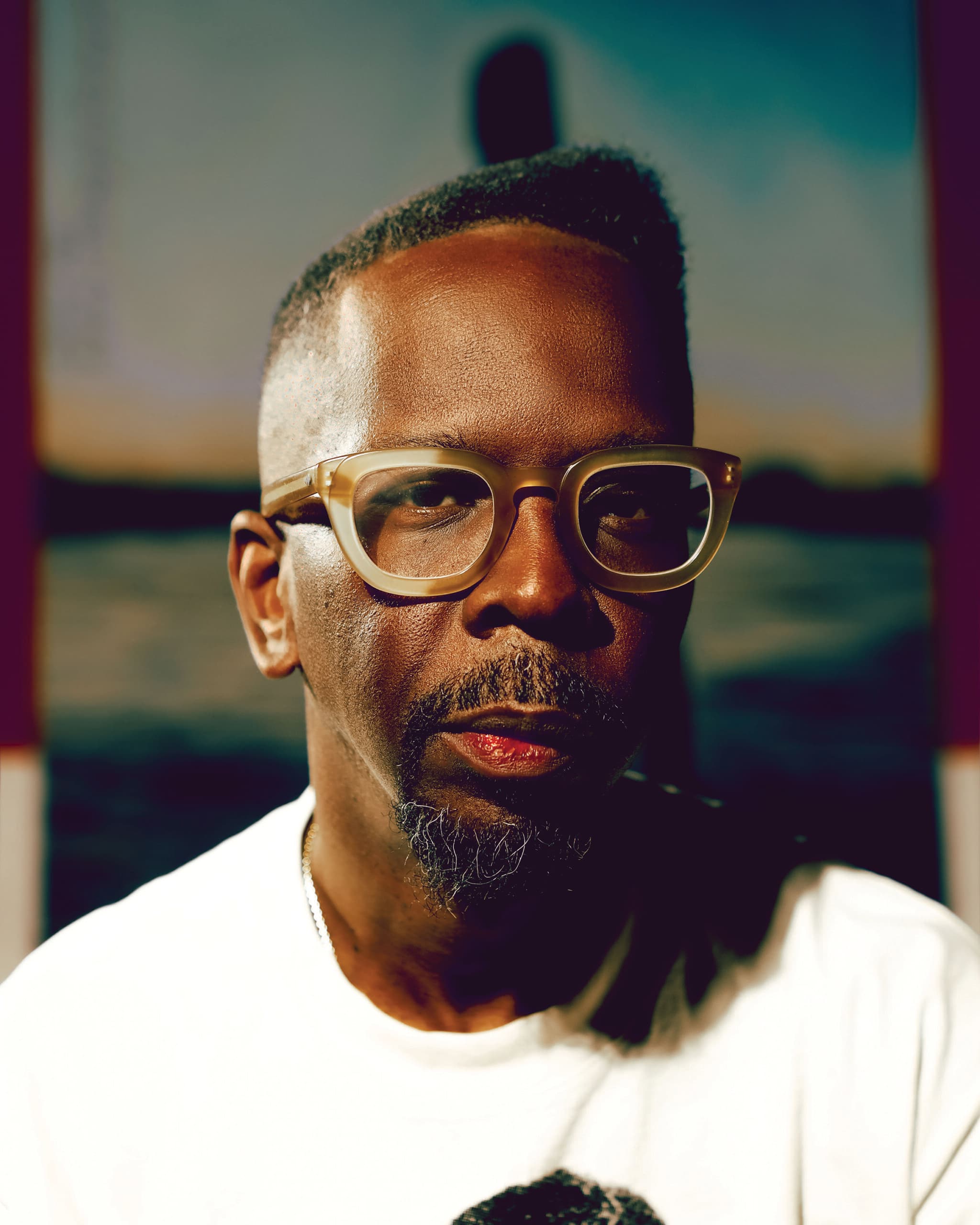 A close-up shot of Fahamu Pecou, he's wearing tan glasses and looking directly at the camera.