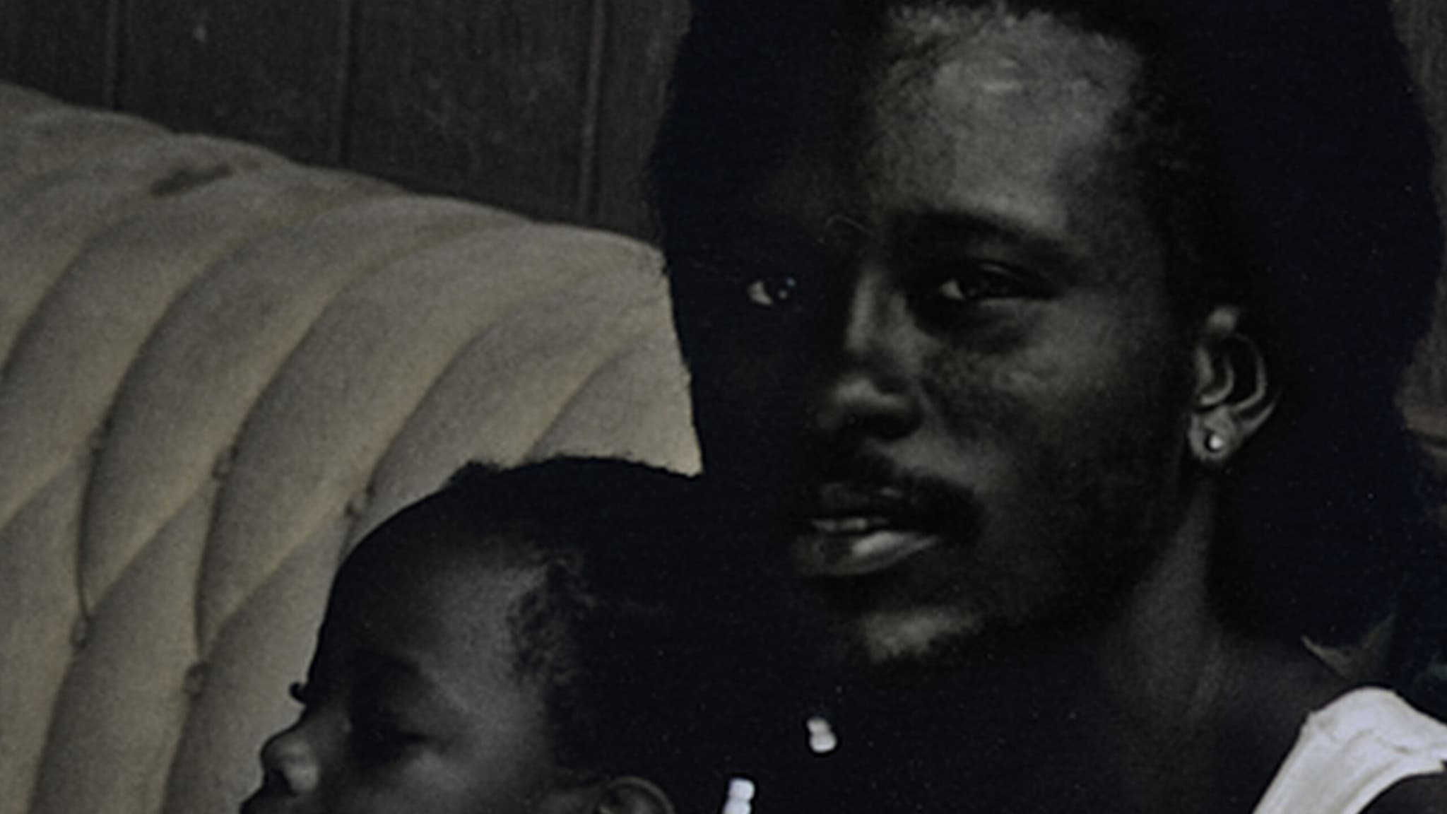 A man looking directly at the camera, with a child on his lap, looking away to the side.